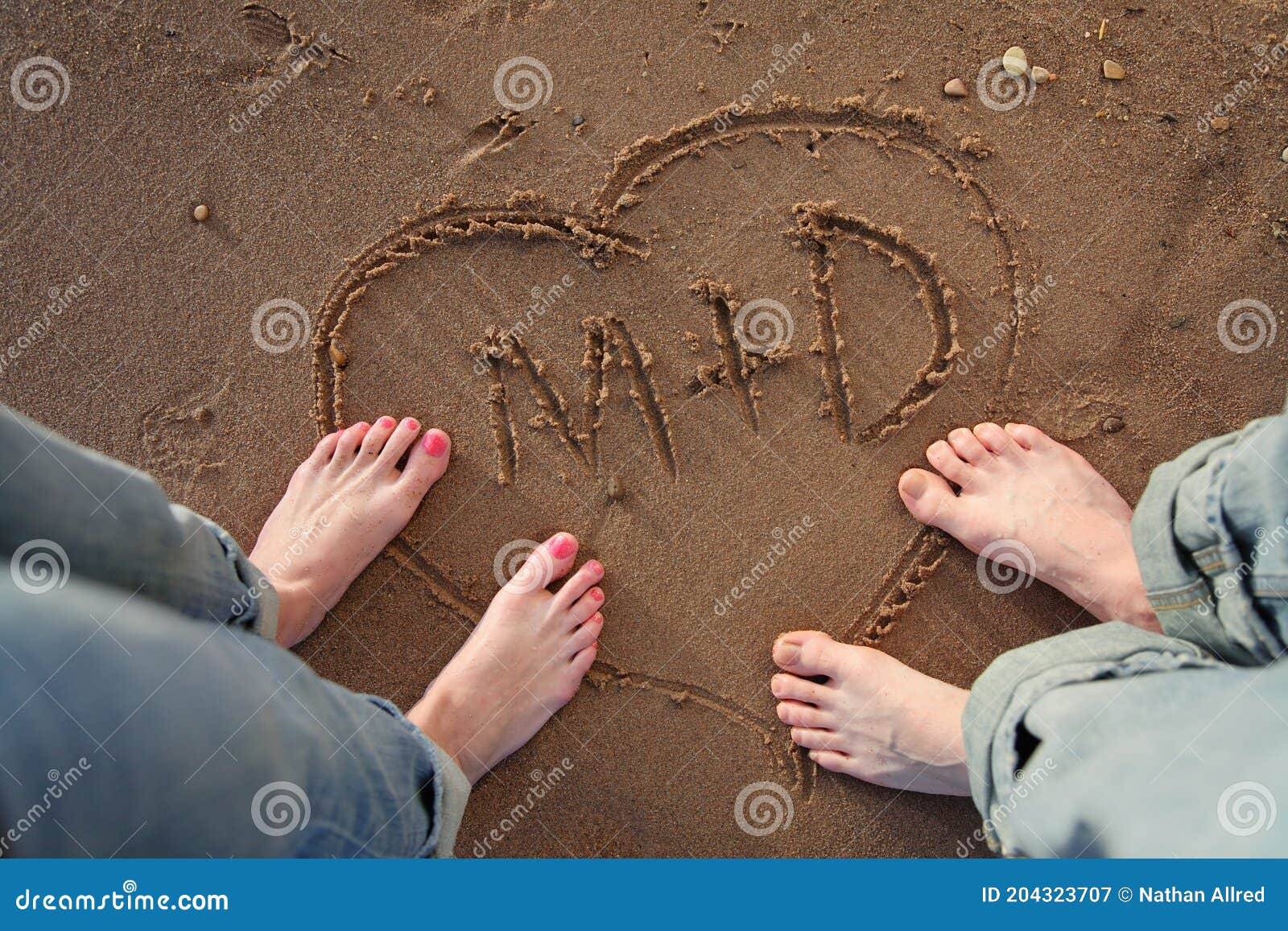 couple standing on beach with heart and initials in sand