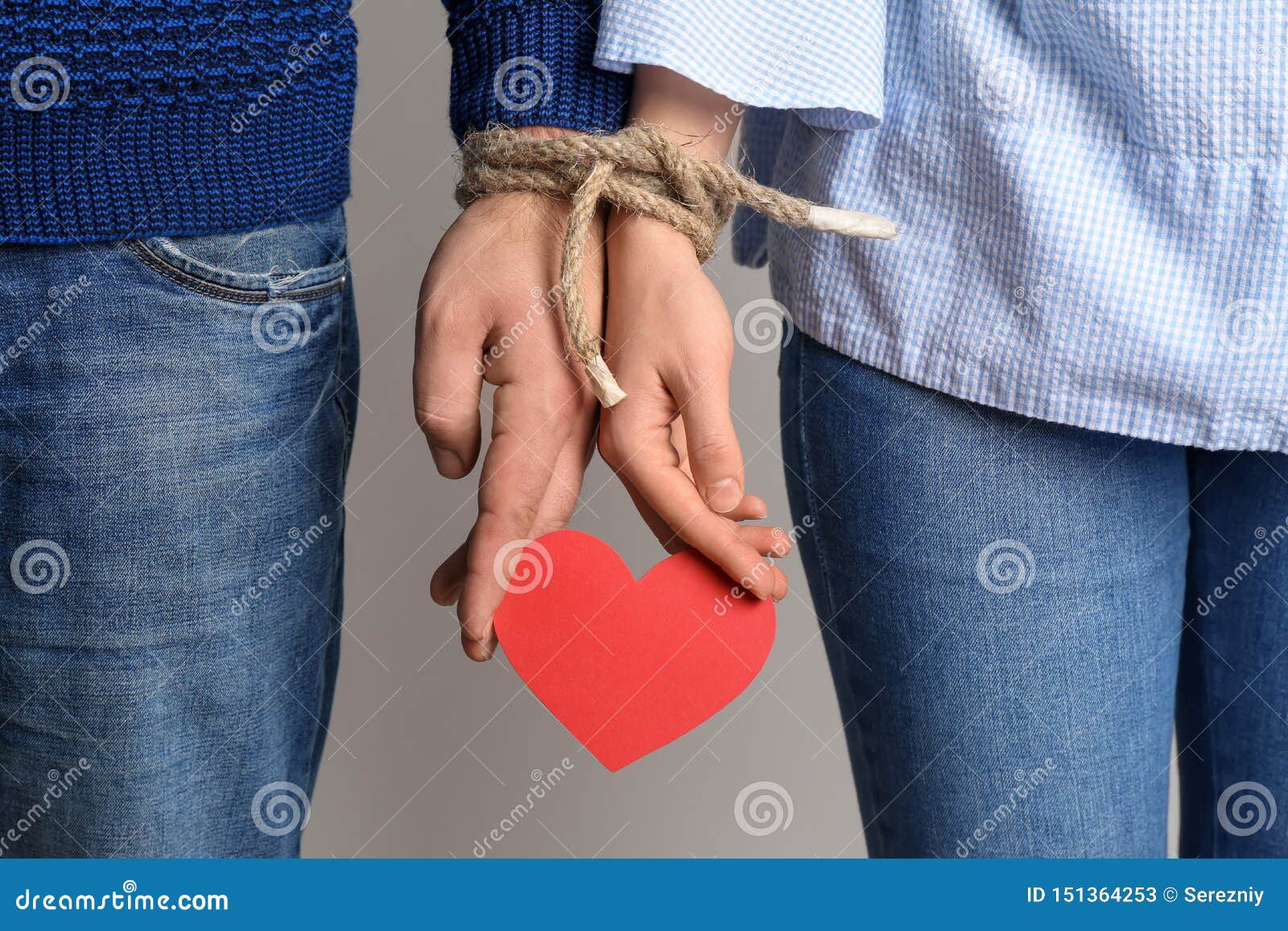 couple with tied together hands holding paper heart on light background. concept of addiction