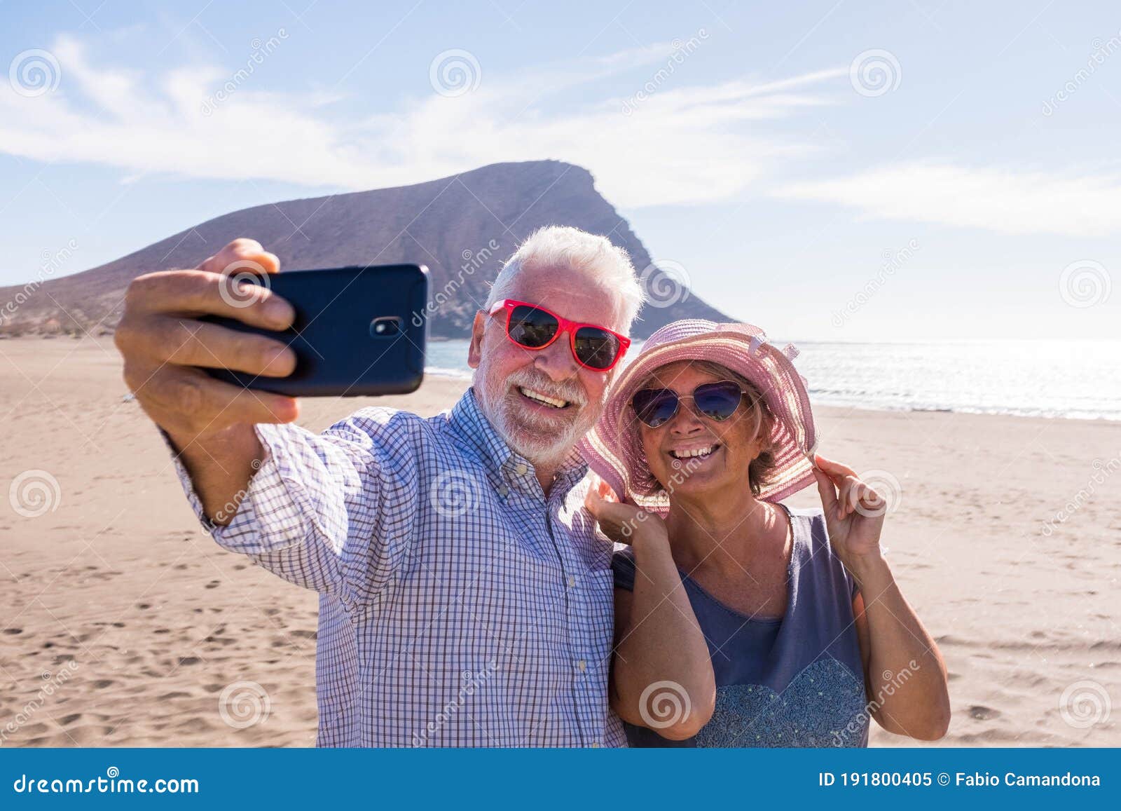 couple of two seniors taking a selfie together at the beach having fun in their vacations - happy mature old people smiling and