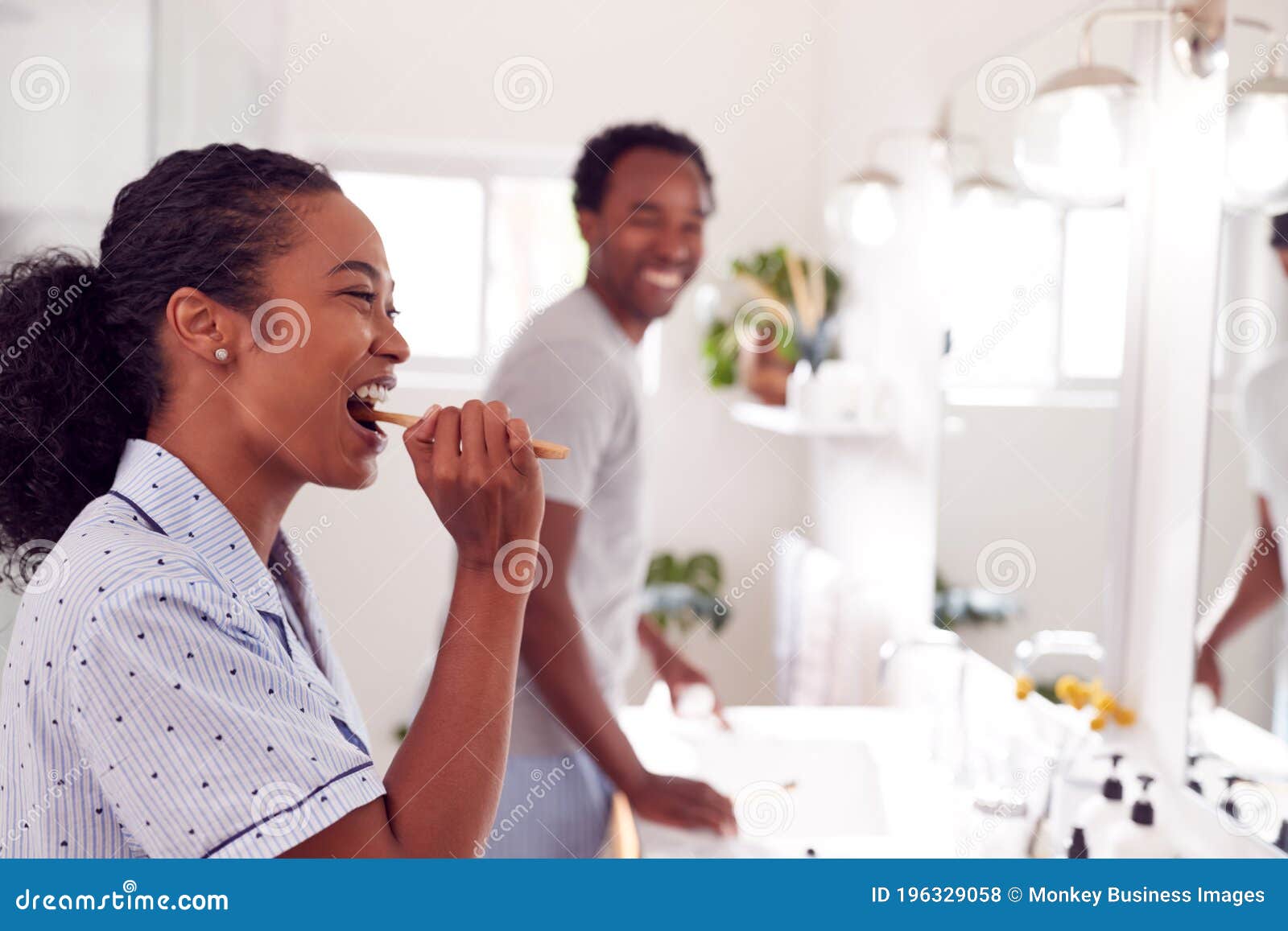 couple wearing pyjamas standing in bathroom at sink brushing teeth in the morning