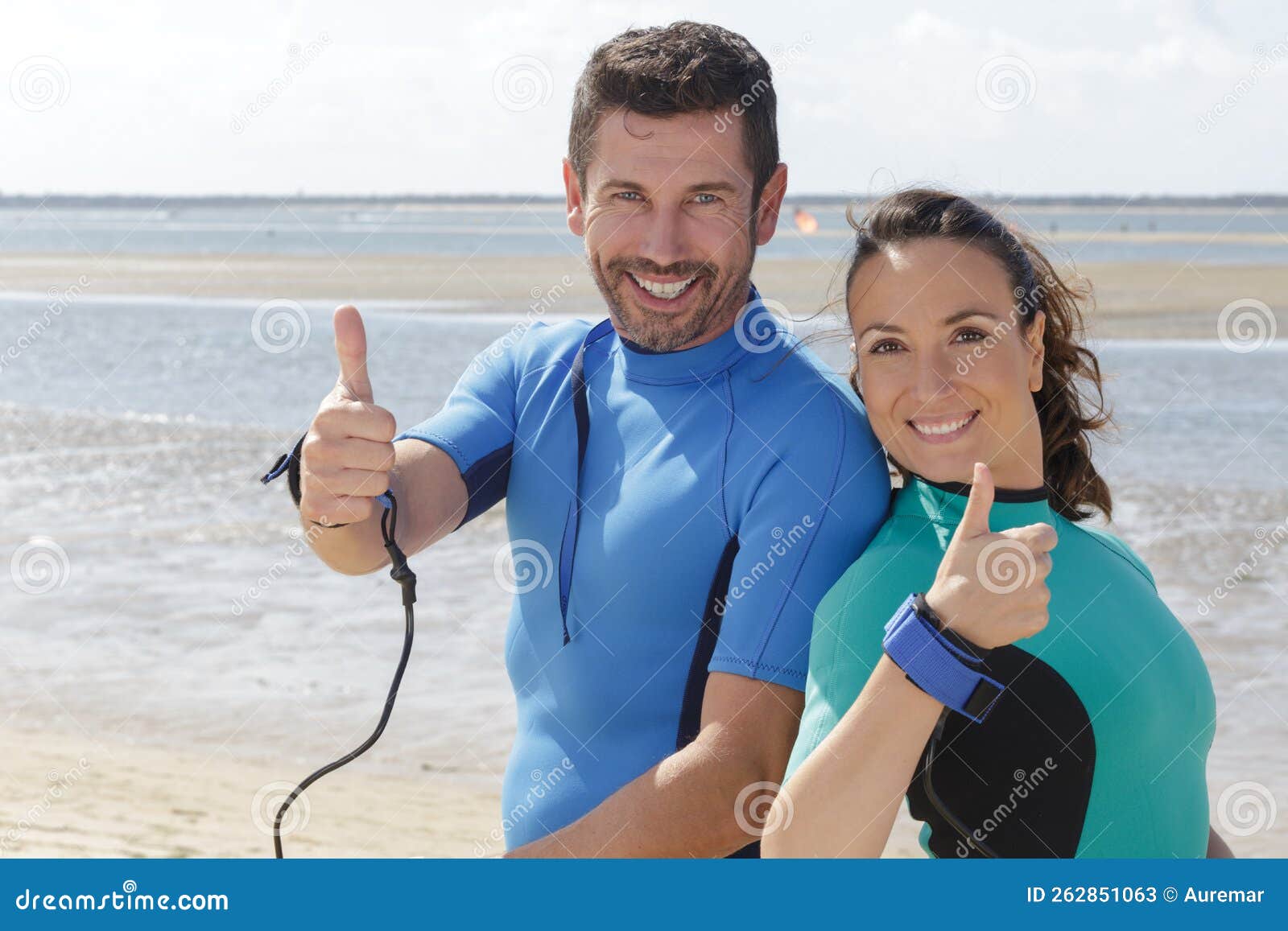 Couple Wearing Wetsuits on Beach Making Thumbs Up Gestures Stock Image