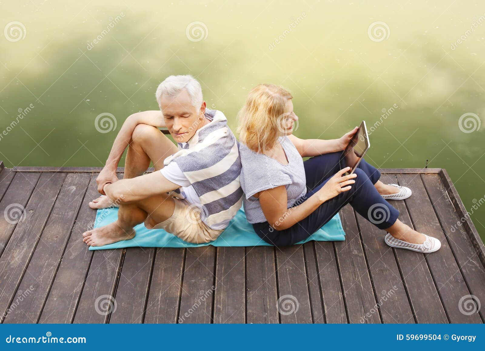 Couples aînés Relaxed. Portrait des couples supérieurs se reposant de nouveau au dos sur le pilier tandis qu'eldely femmes se tenant dans son comprimé numérique de main touchant l'écran