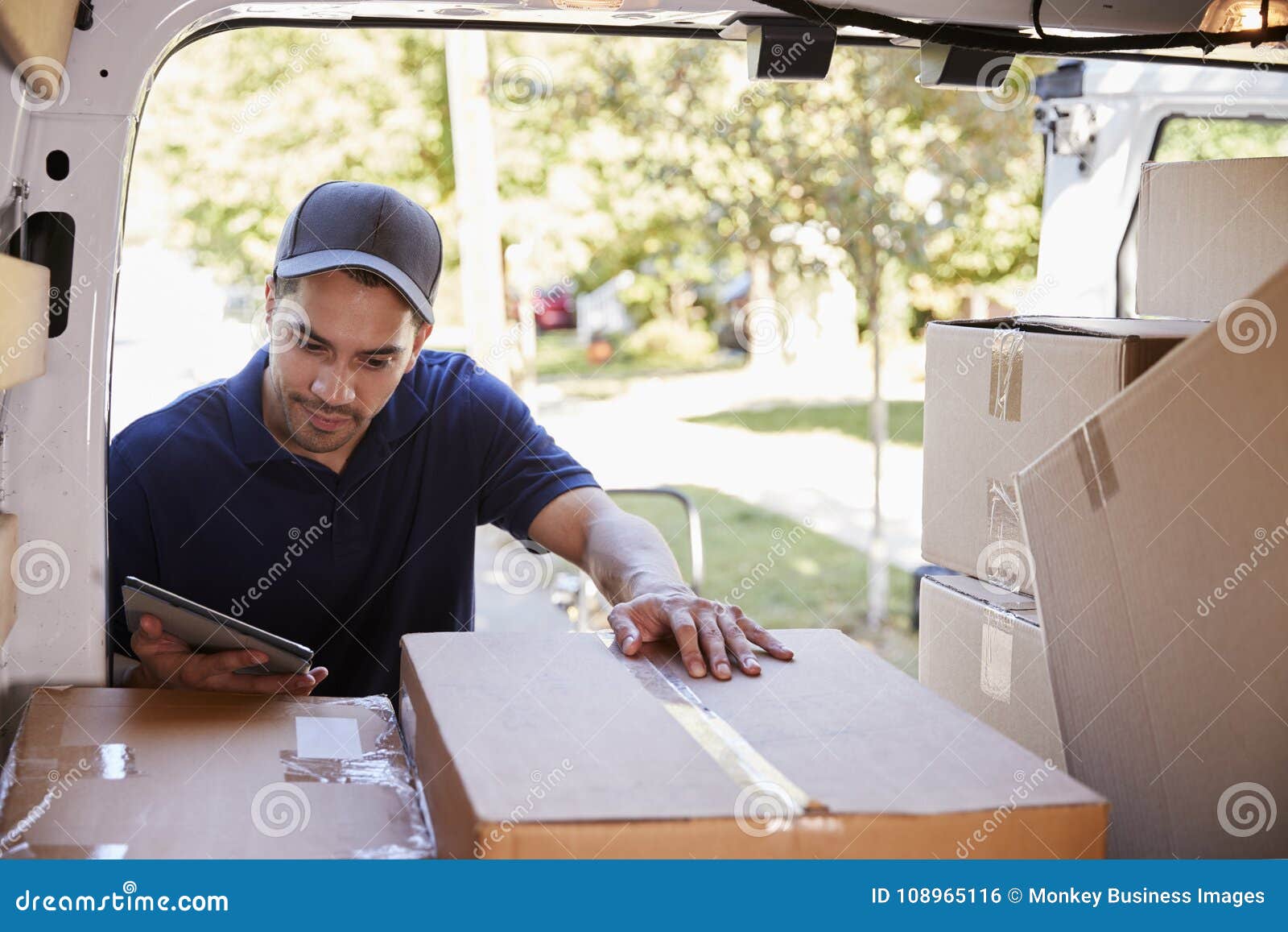 Courier with Digital Tablet Checking Packages in Van Stock Photo