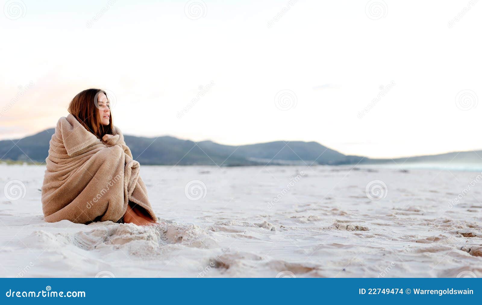 Couverture froide de plage. La femme froide enveloppe la couverture au-dessus du hersolf tout en se reposant sur la plage après coucher du soleil. le copyspace a fourni par image panoramique