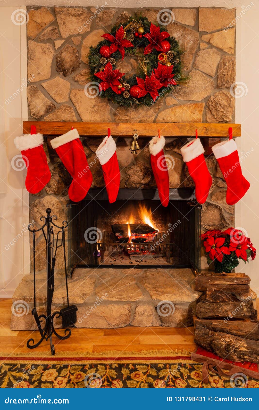 fireplace with six christmas stockings, logs, bells and wreath.