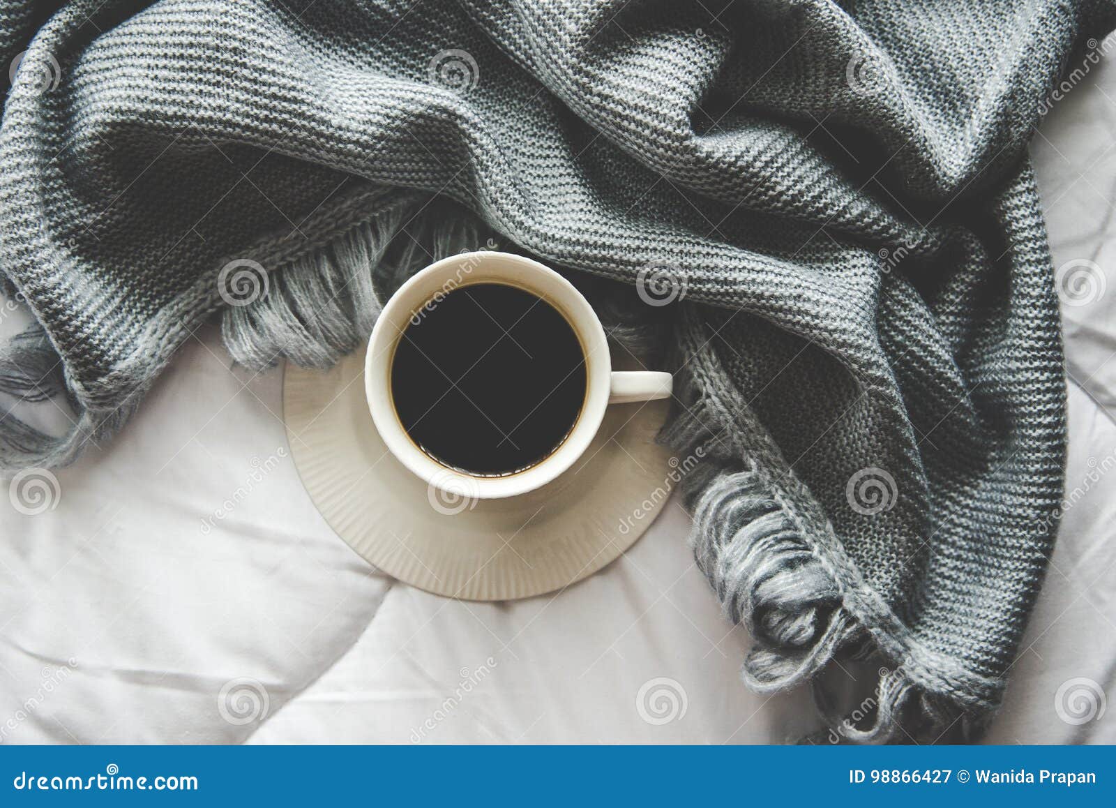 cozy winter home background, cup of hot coffee with marshmallow, warm knitted sweater on white bed background, vintage tone.