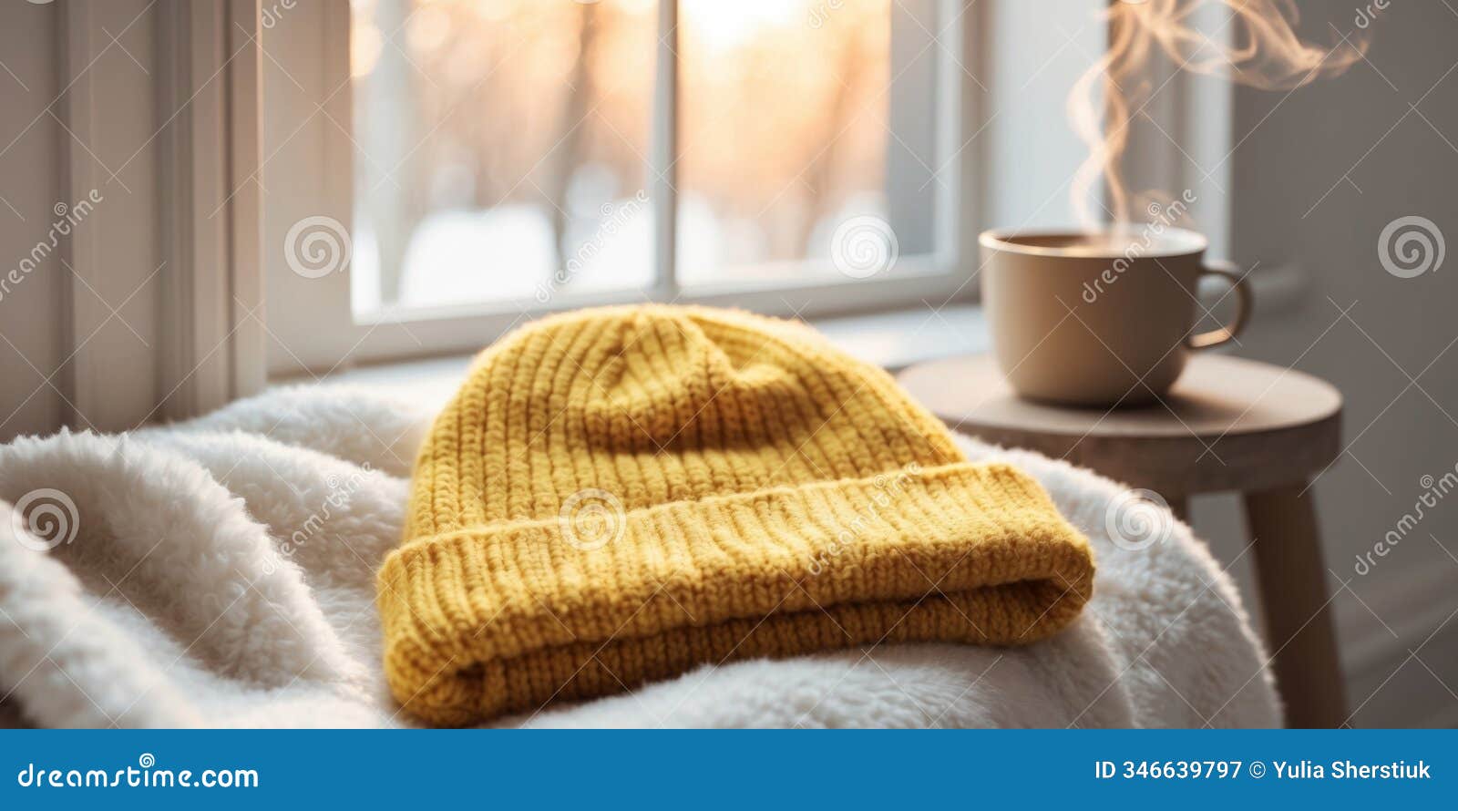 cozy winter scene featuring a yellow knit beanie on soft white blanket by a sunlit window with a warm beverage in the