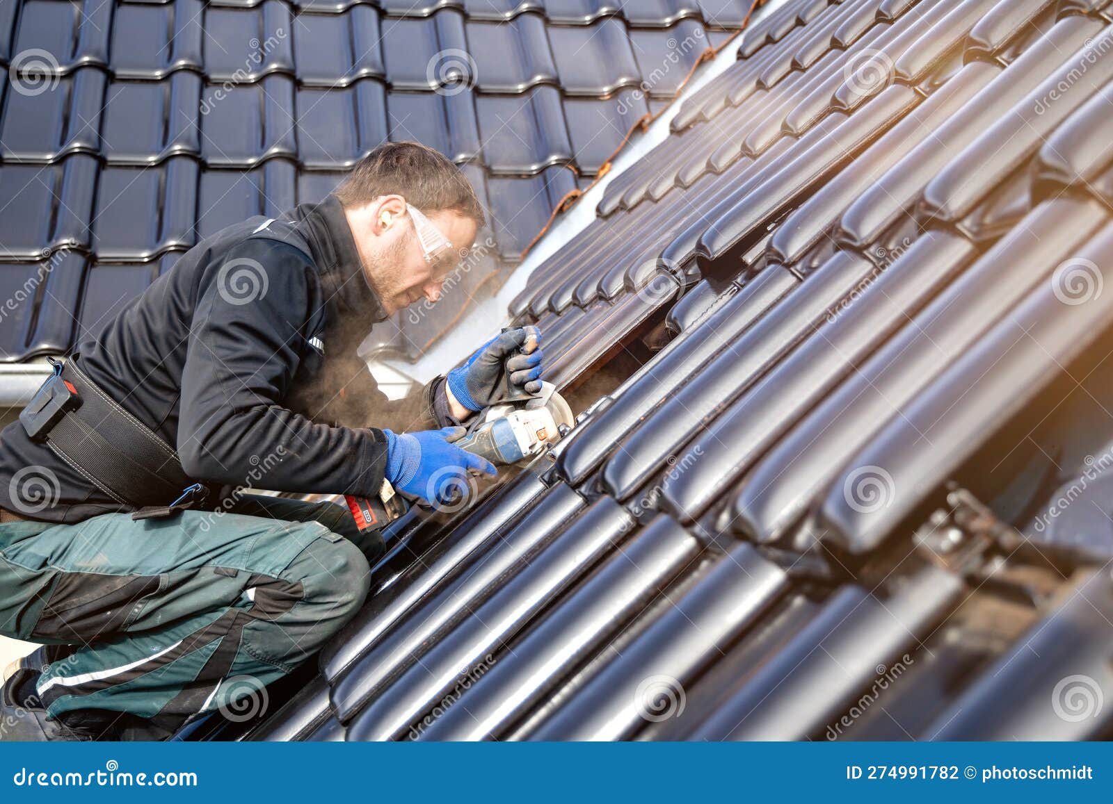 Craftsman Using an Angle Grinder To Cut a Tile on a Roof Stock Photo