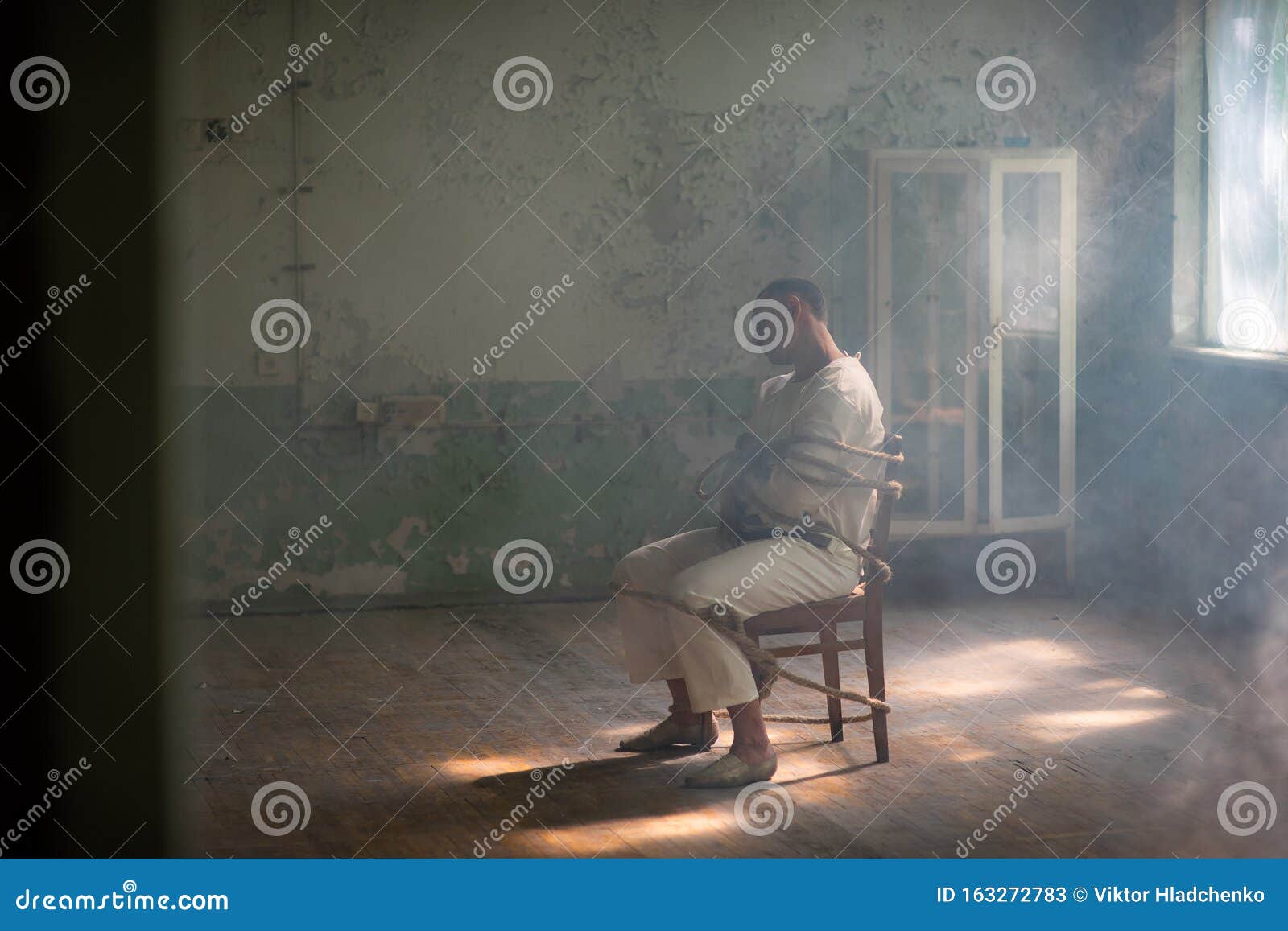 a crazy man in a straitjacket is tied to a chair in an abandoned old clinic