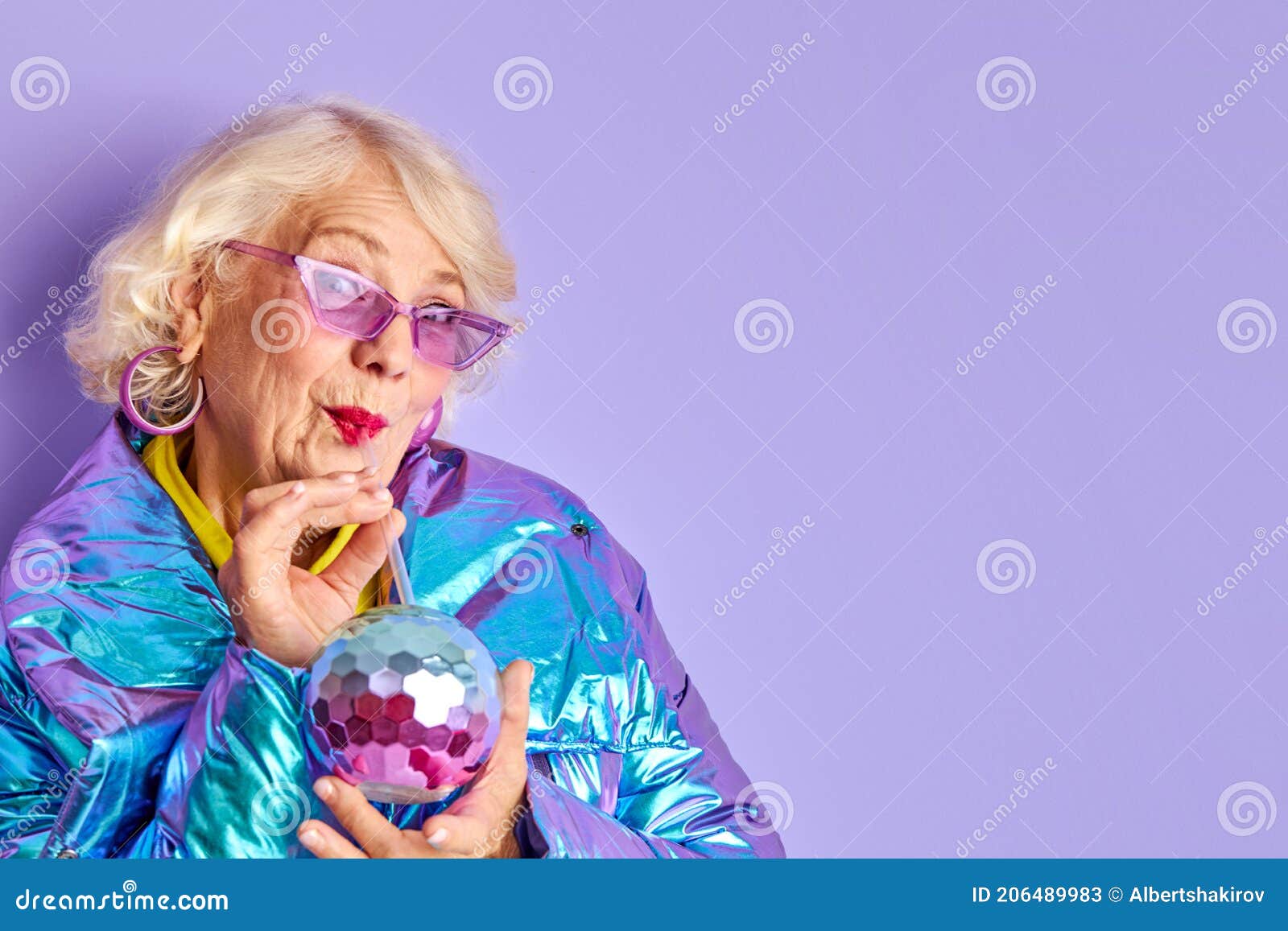 Crazy stylish woman drink beverage from colourful bottle. Woman drink beverage from colourful bottle, party time. senior lady im blue coat and stylish sunglasses posing at camera