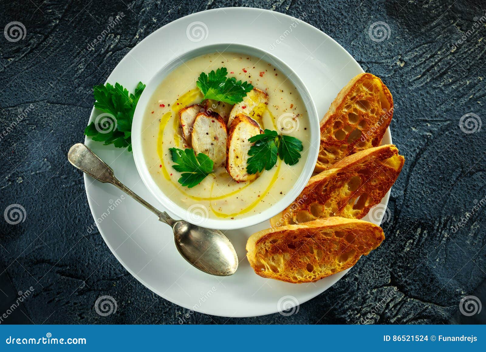 creamy chicken soup with vegetables in bowl with chiabatta toast, parsley and nigela seeds sprinkle on stone table