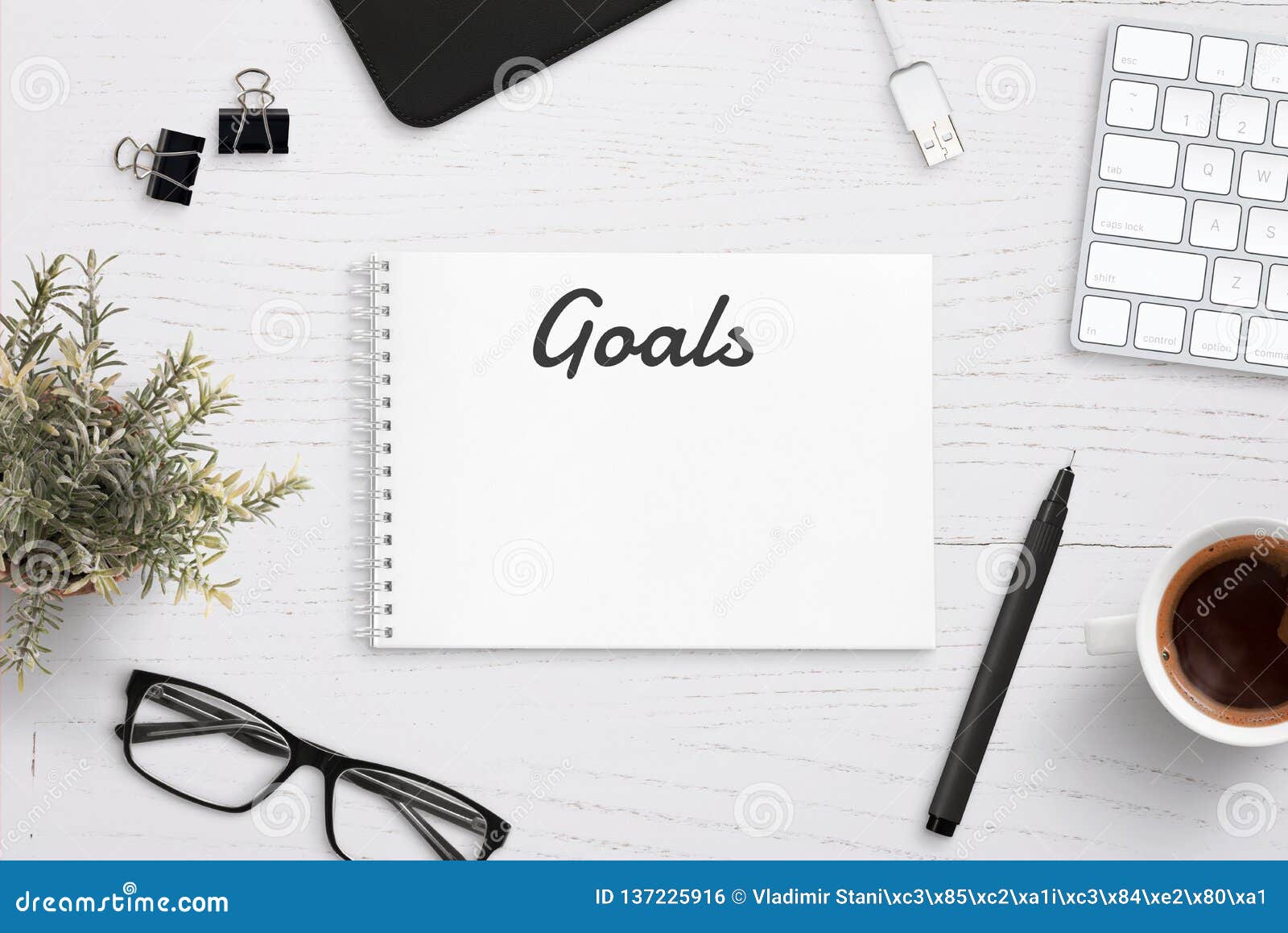 Creating Goals List On Notepad On Office Desk Surrounded With