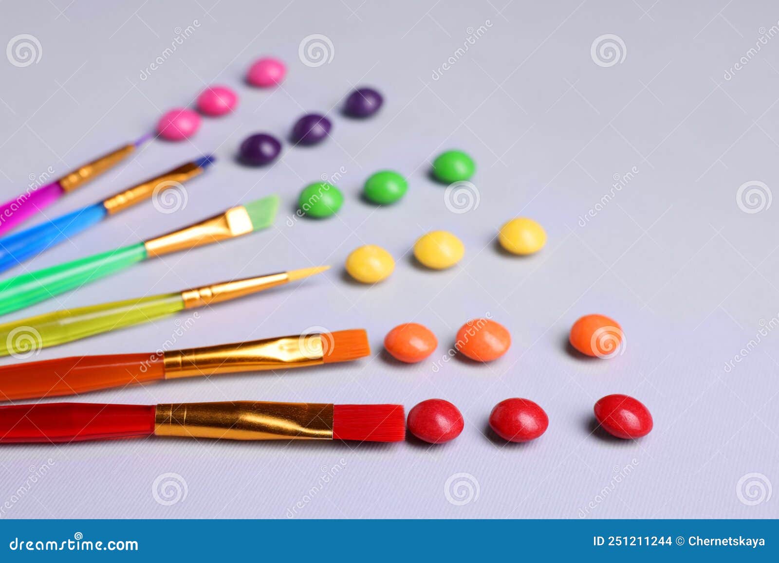 Creative Composition with Paint Brushes and Colorful Candies on Light