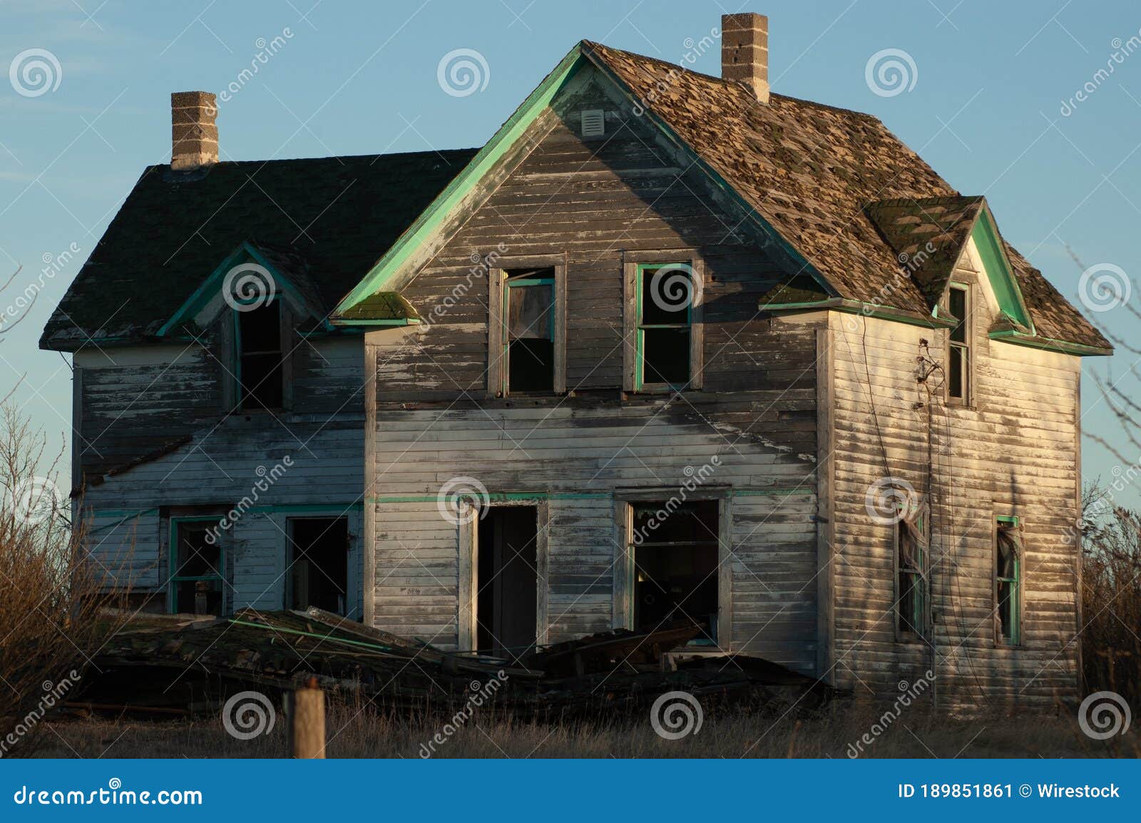 creepy, old and aged abandoned wooden house in a field under the blue sky