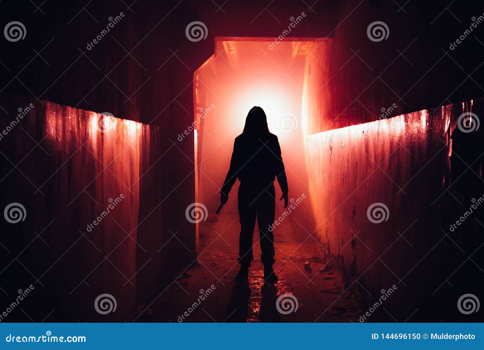 creepy silhouette with knife in the dark red illuminated abandoned building. horror about maniac concept
