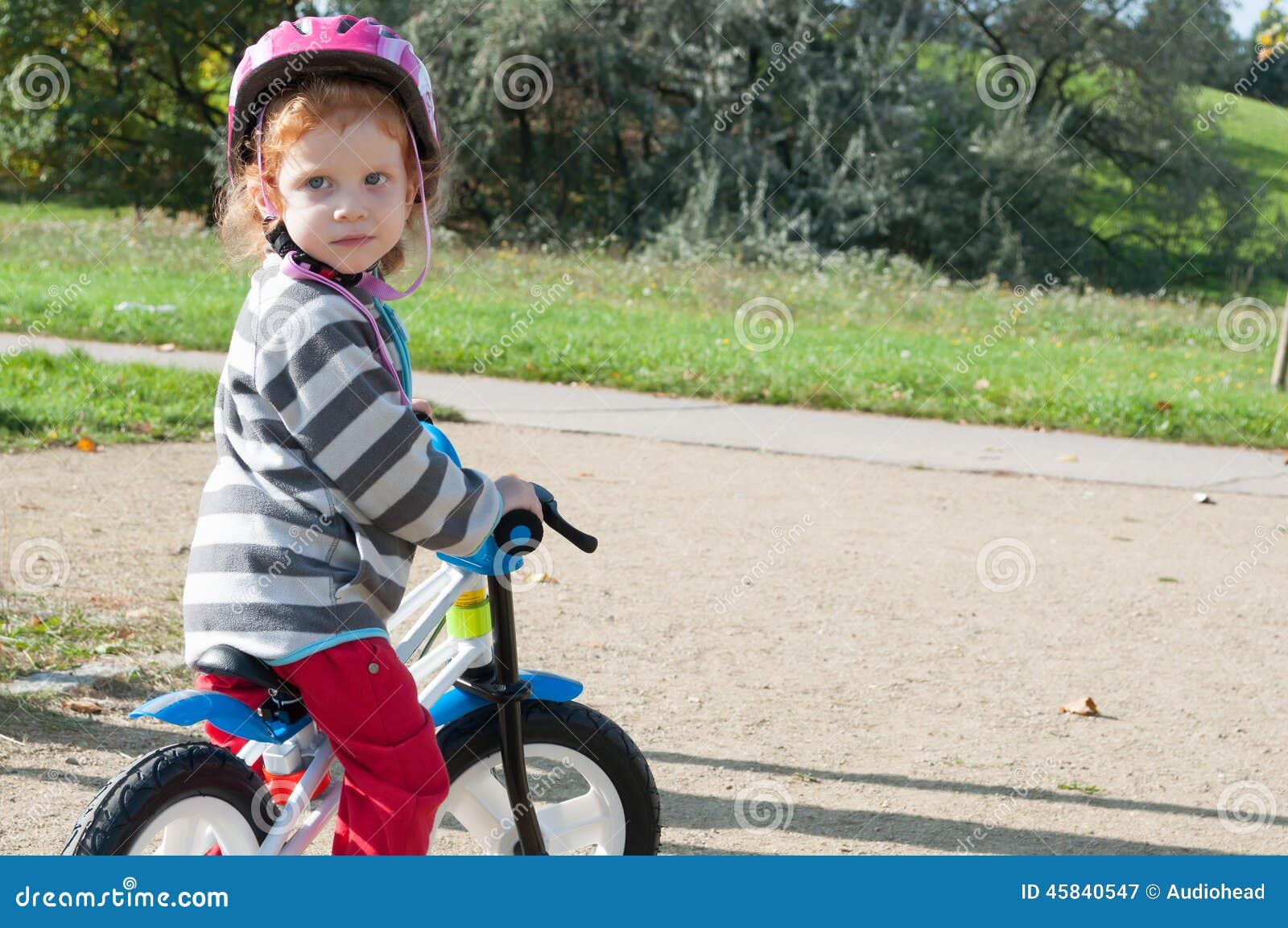 Criança com bicicleta. Menina da criança com o capacete de segurança na bicicleta no parque do outono