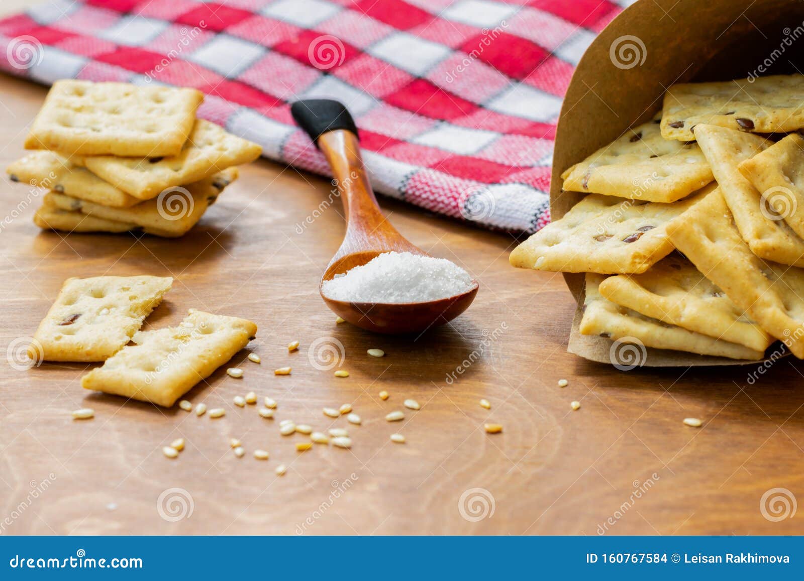 crispy salted crackers, wooden spoon with salt crystalls, paper bag full of crackers on a red napkin on wooden table.