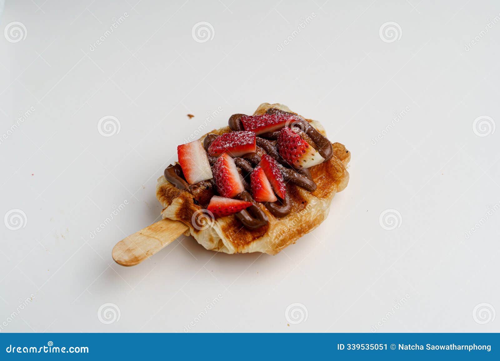 a croissant waffle or croffle with chocolate sauce, strawberries slices and cocoa powder on top