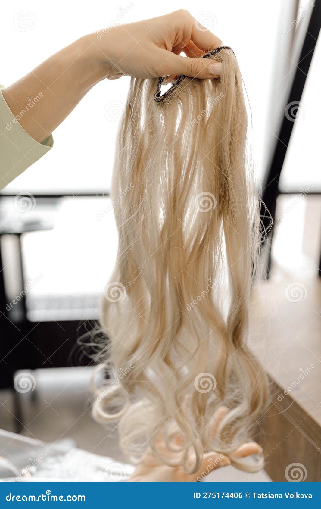 cropped photo of woman hairdresser holding long fair blond hairpiece chignon weave bundle for extension in beauty salon.