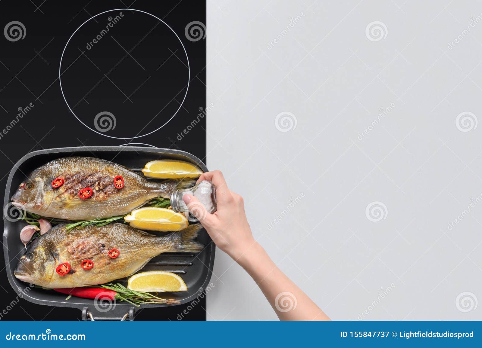 Cropped Shop of Person Adding Salt while Cooking Fish Stock Image