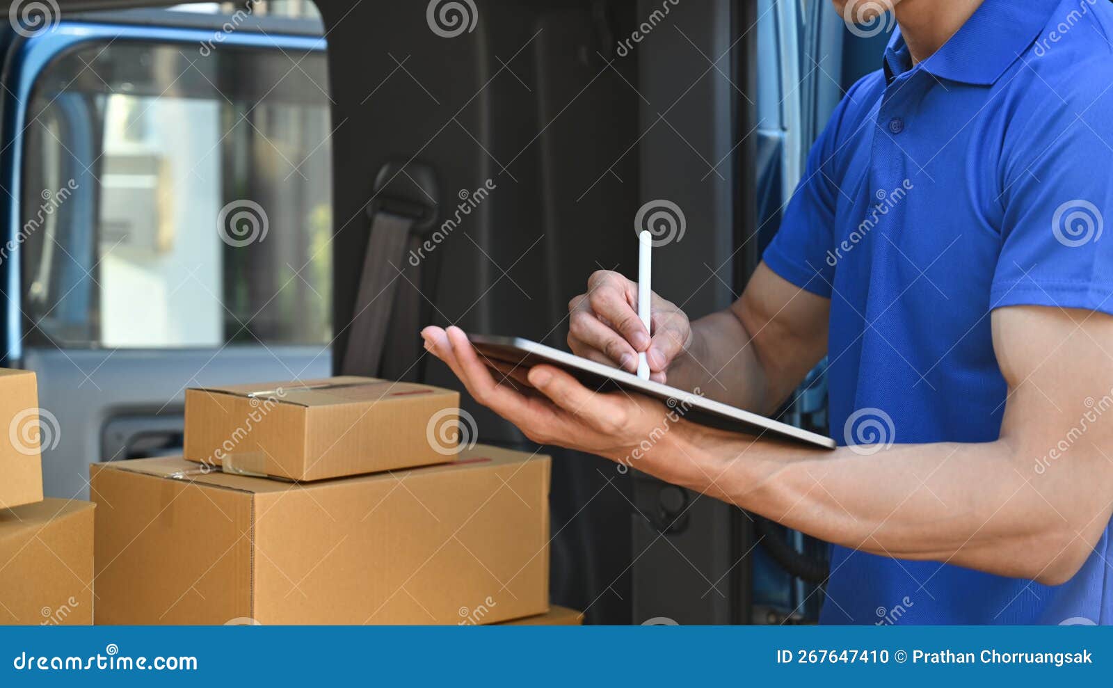 cropped shot of delivery man in blue uniform using digital tablet next to open delivery van. shipping and delivery