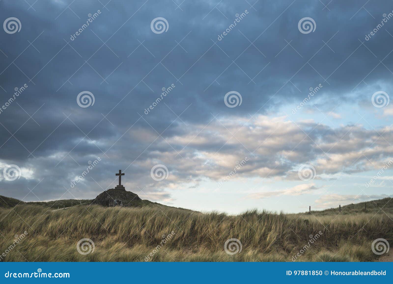cross in landscape of ynys llanddwyn island at sunset with moody