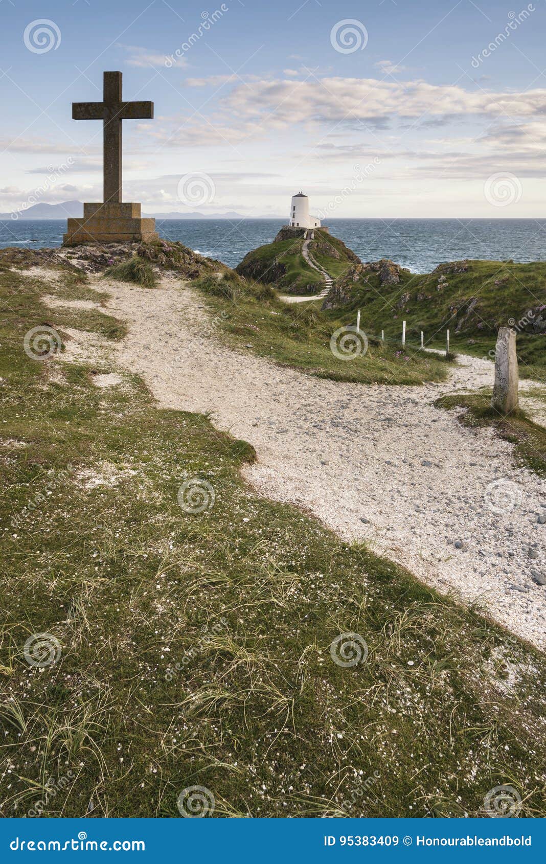 cross in landscape of ynys llanddwyn island with twr mawr lighthouse in background with blue sky