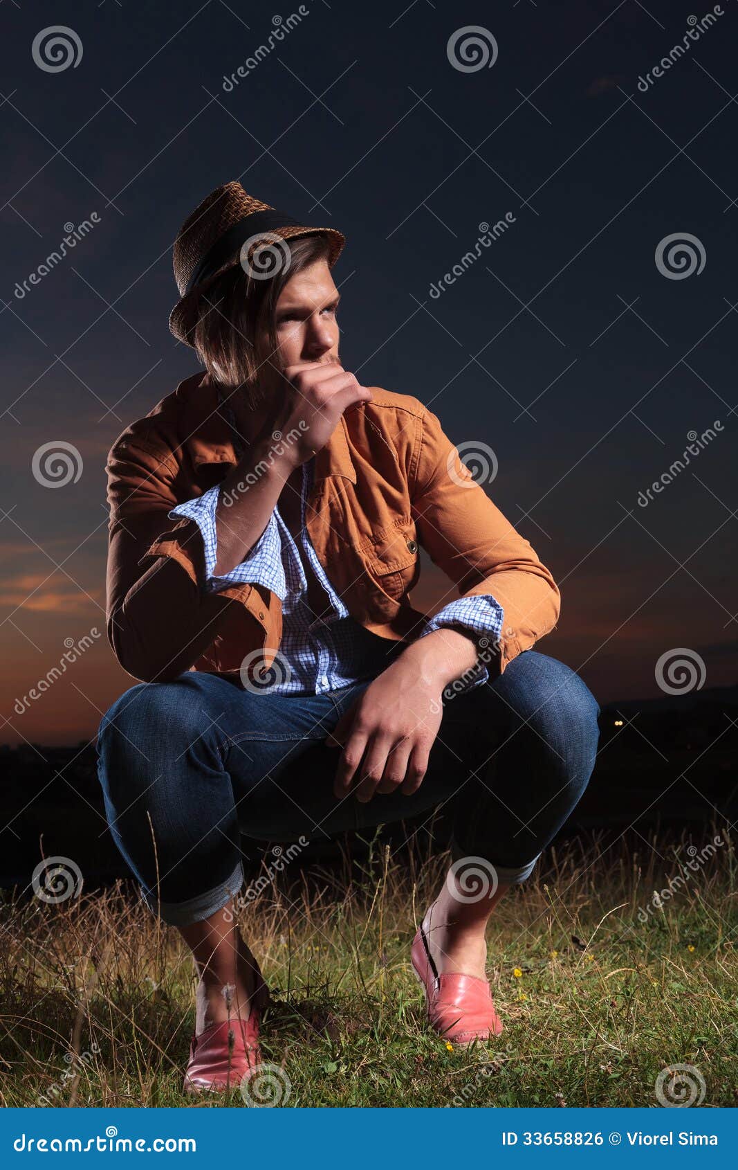 crouched casual man holds straw in mouth