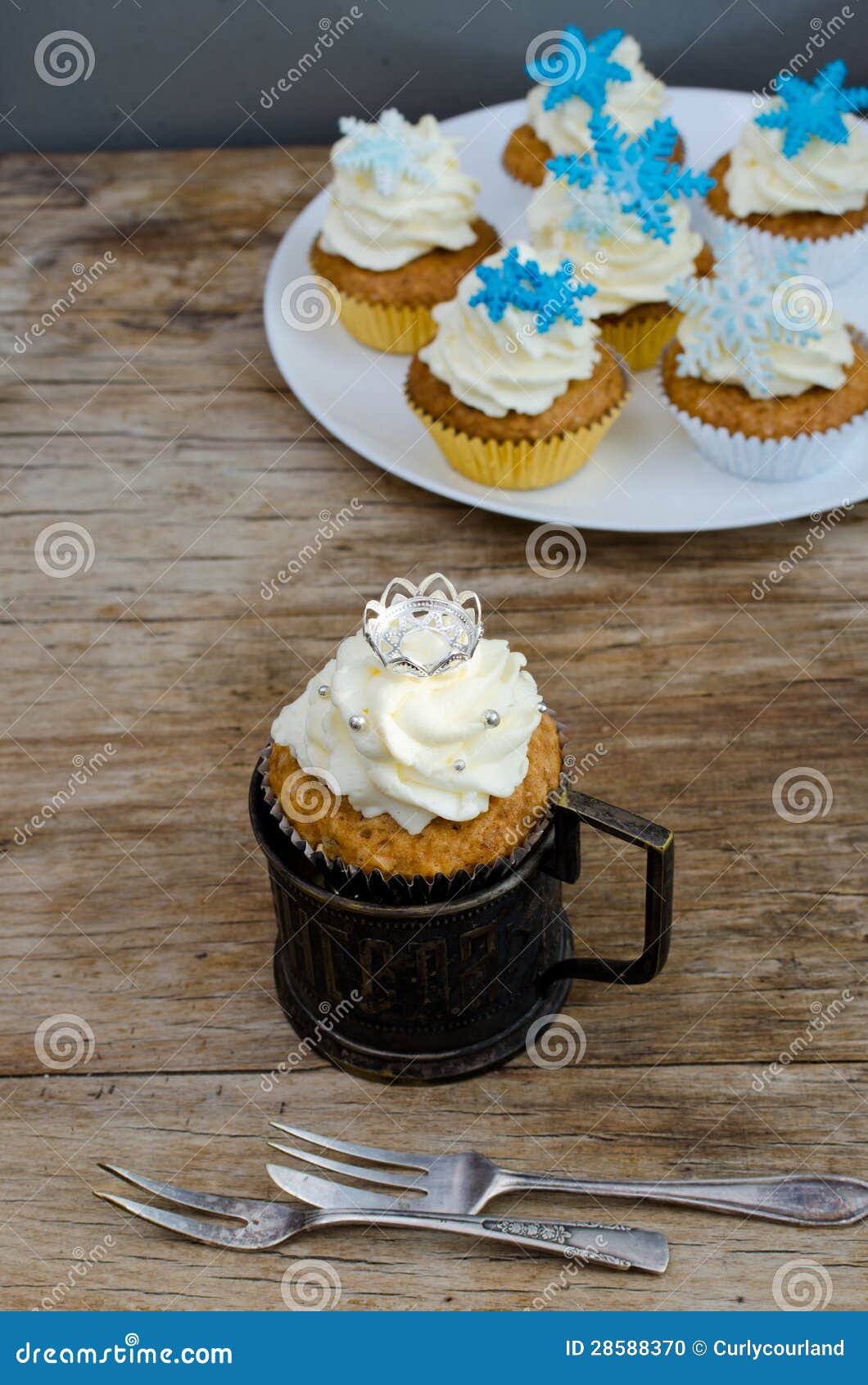 Crown And Snowflakes Muffins. Orange walnut muffins with sour-cream frosting into the silver glass-holders with silver dessert forks on the vintage wooden table. Crown and snowflakes decor.