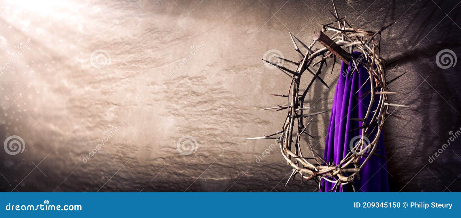 crown of thorns and purple robe hanging on nail in stone wall with light rays