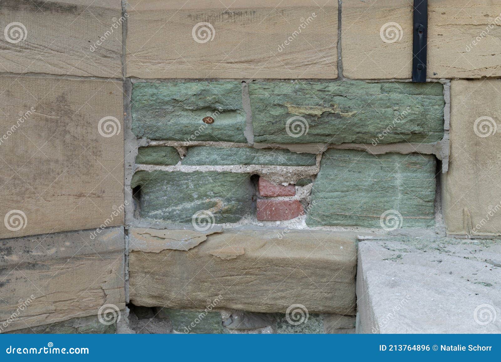 crumbling and eroded tan and green limestone wall revealing brick behind and sturdier mortar, effects of acid rain