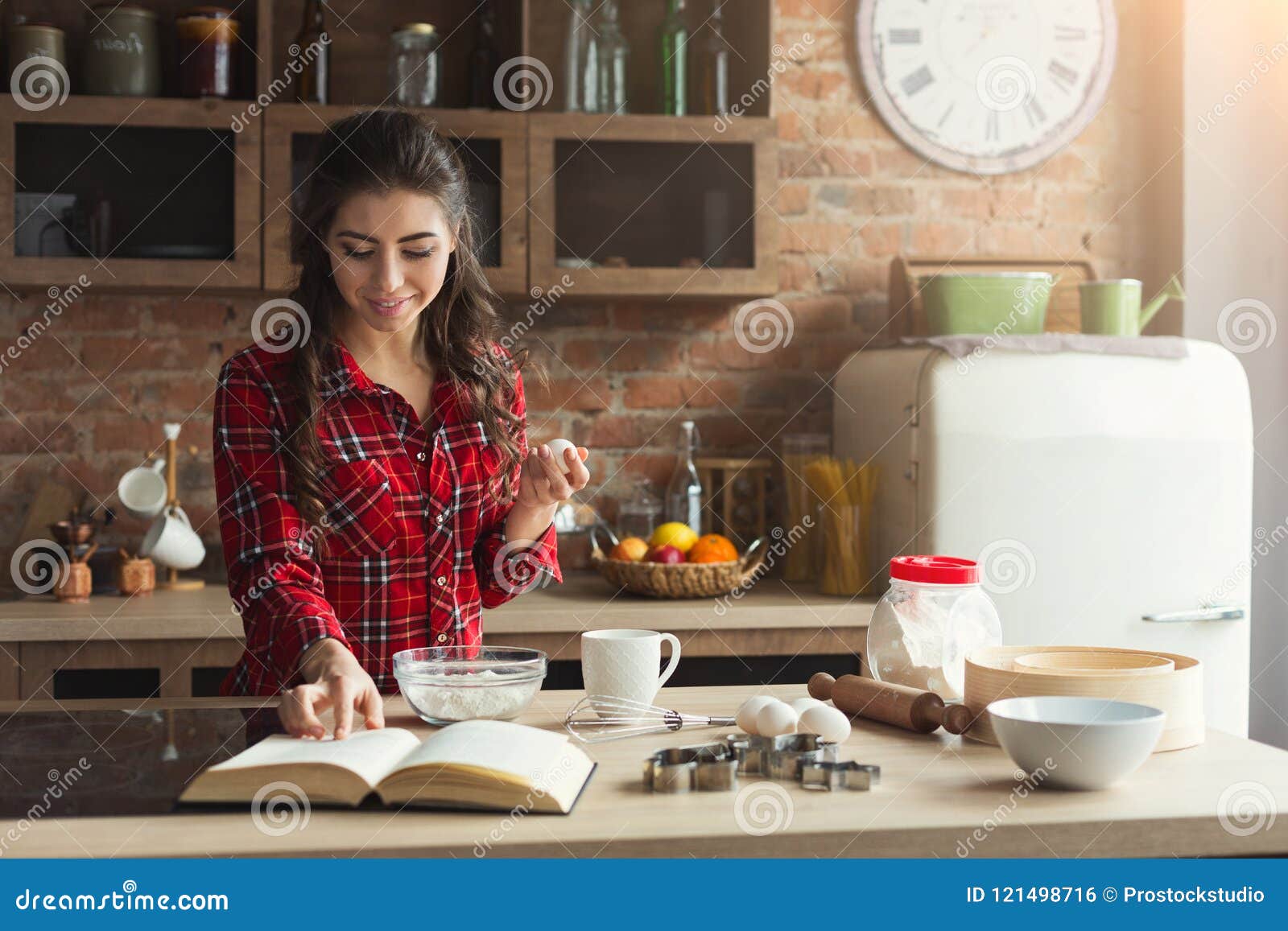 Cuisson heureuse de jeune femme dans la cuisine de grenier. Tarte heureux de cuisson de jeune femme dans la cuisine de grenier à la maison, utilisant le livre avec la recette, l'espace de copie