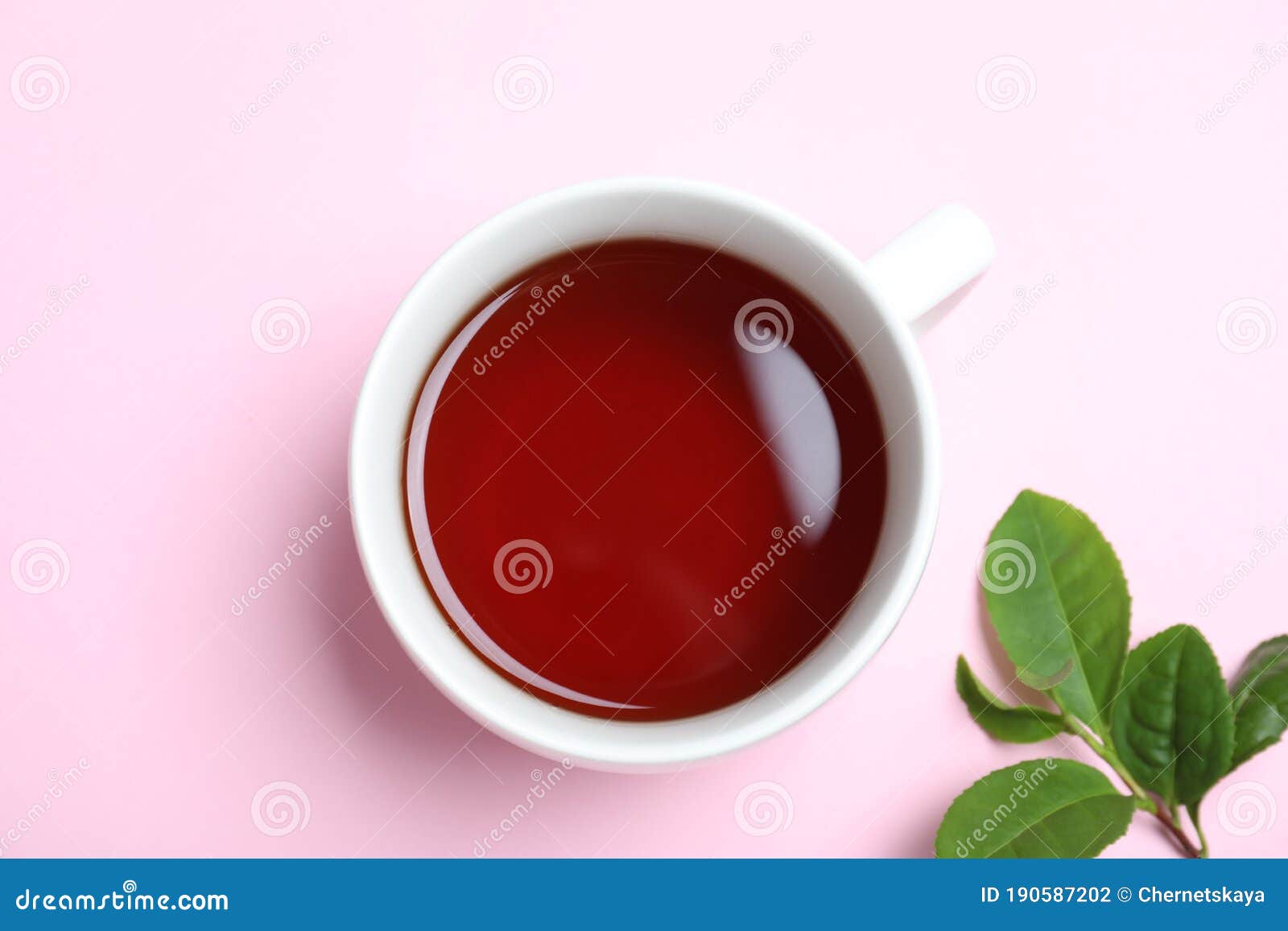 Cup of Aromatic Black Tea and Green Leaves on Background, Flat Lay