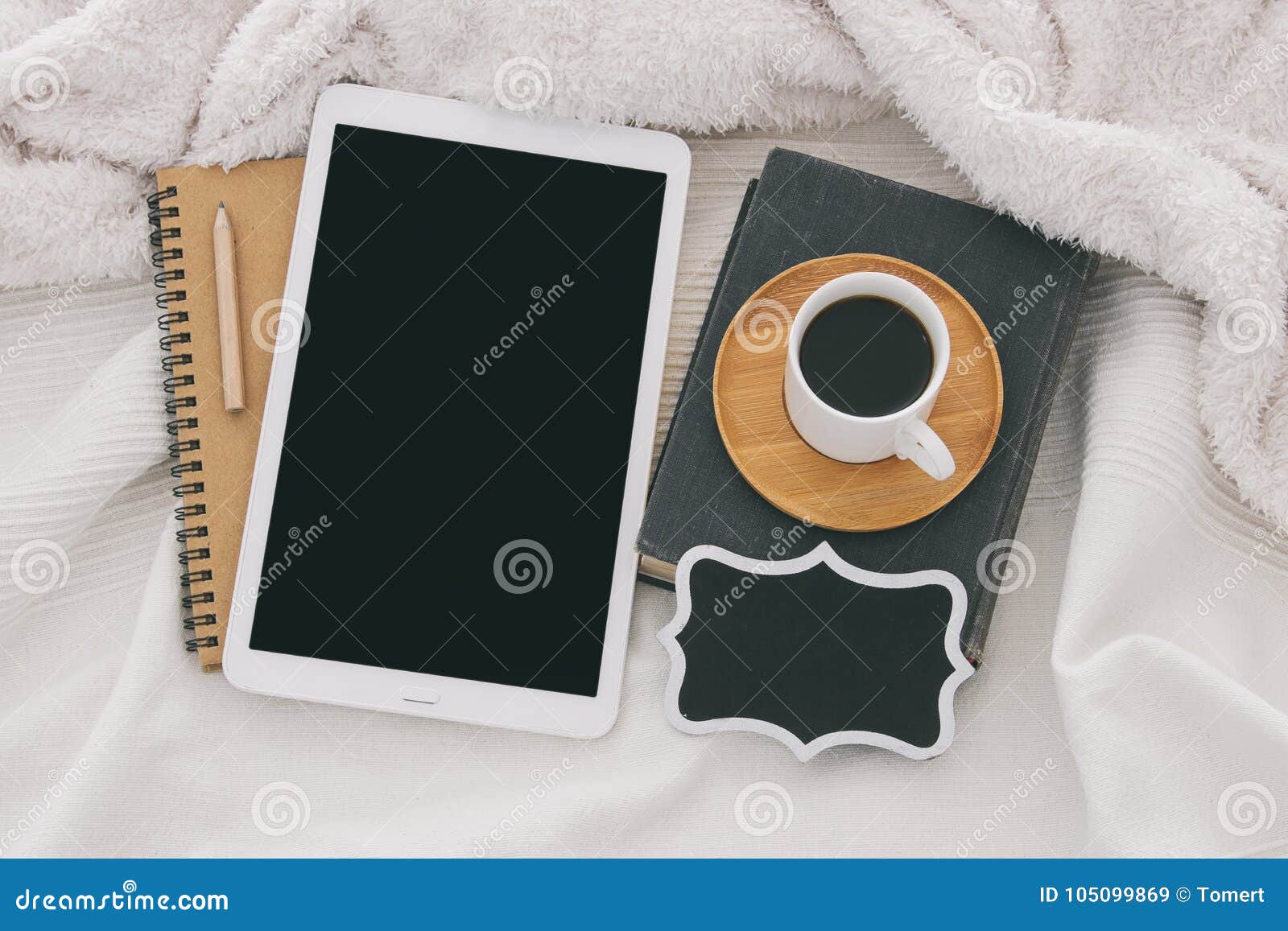 cup of coffee on the old book and tablet device with empty black screen over cozy and white blanket. top view.