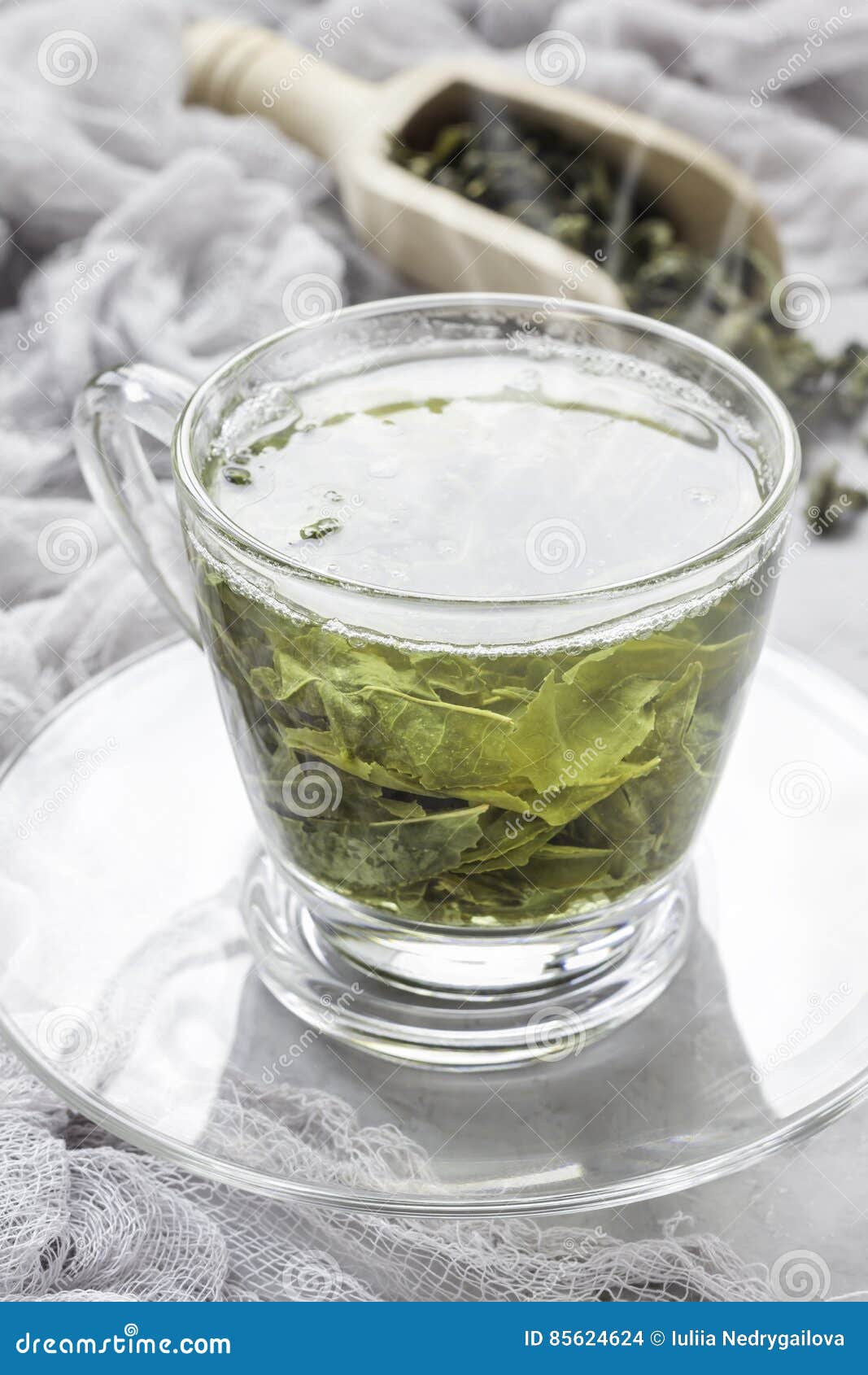 Cup of Fresh Made Hot Green Tea with Smoke, Dry Leaves on Background