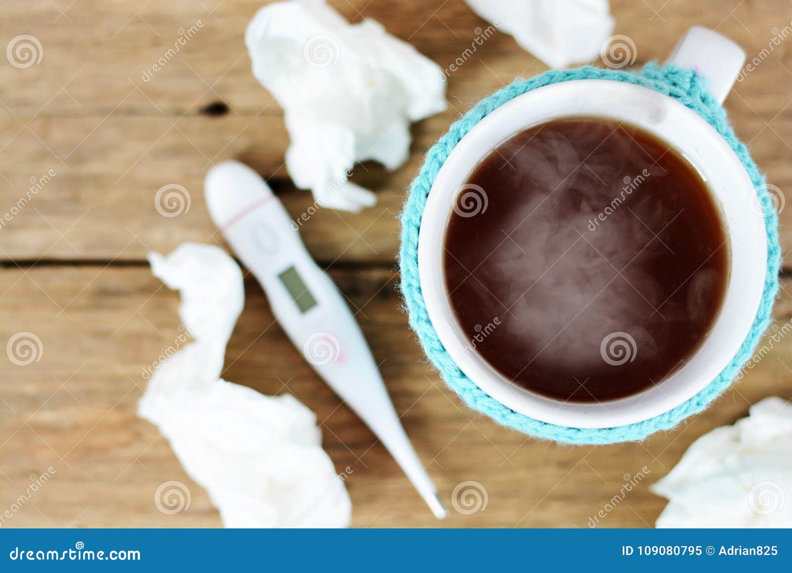 cup of hot tea, paper wipes and thermometer on wooden table suggesting flu season