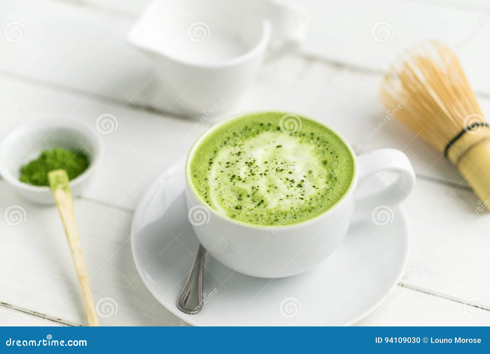 cup of matcha green tea latte with accessories in background.
