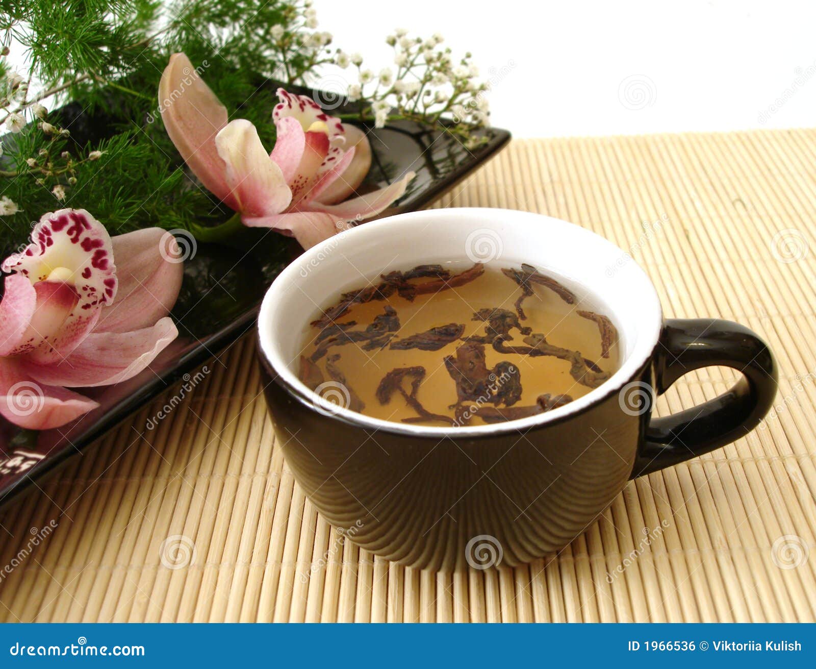 cup of tea with pink orchids on black plate over straw matt