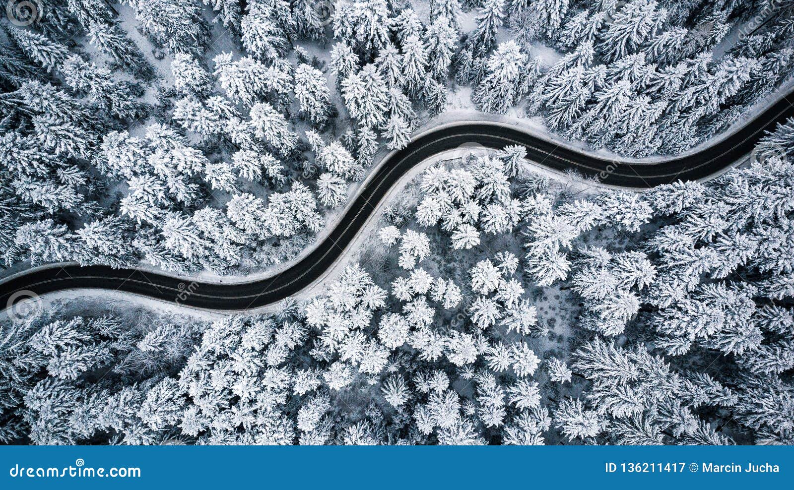 curvy windy road in snow covered forest, top down aerial view