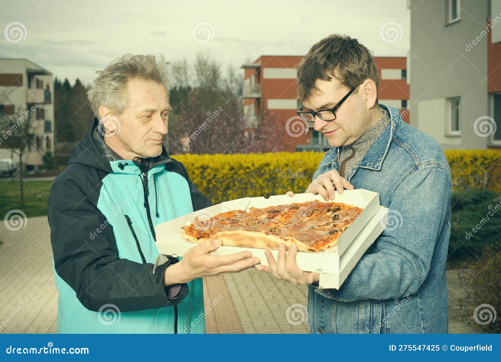 customer assuming a pizza food from a delivery man on sidewalk