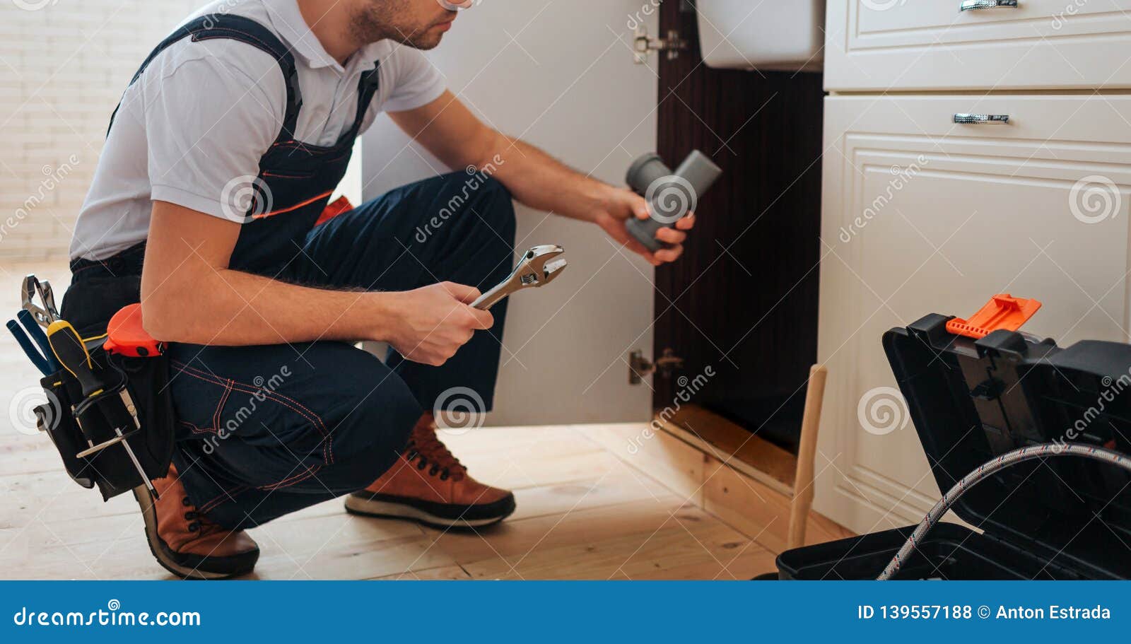 Cut View Of Plumber Sitting In Squad Position In Kitchen He