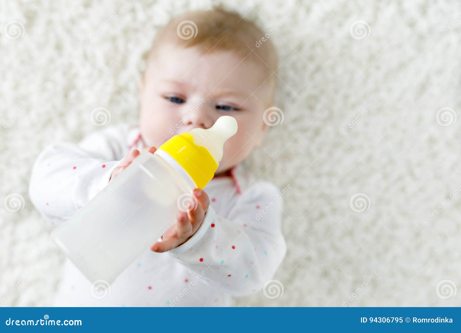 cute adorable ewborn baby girl holding nursing bottle and drinking formula milk