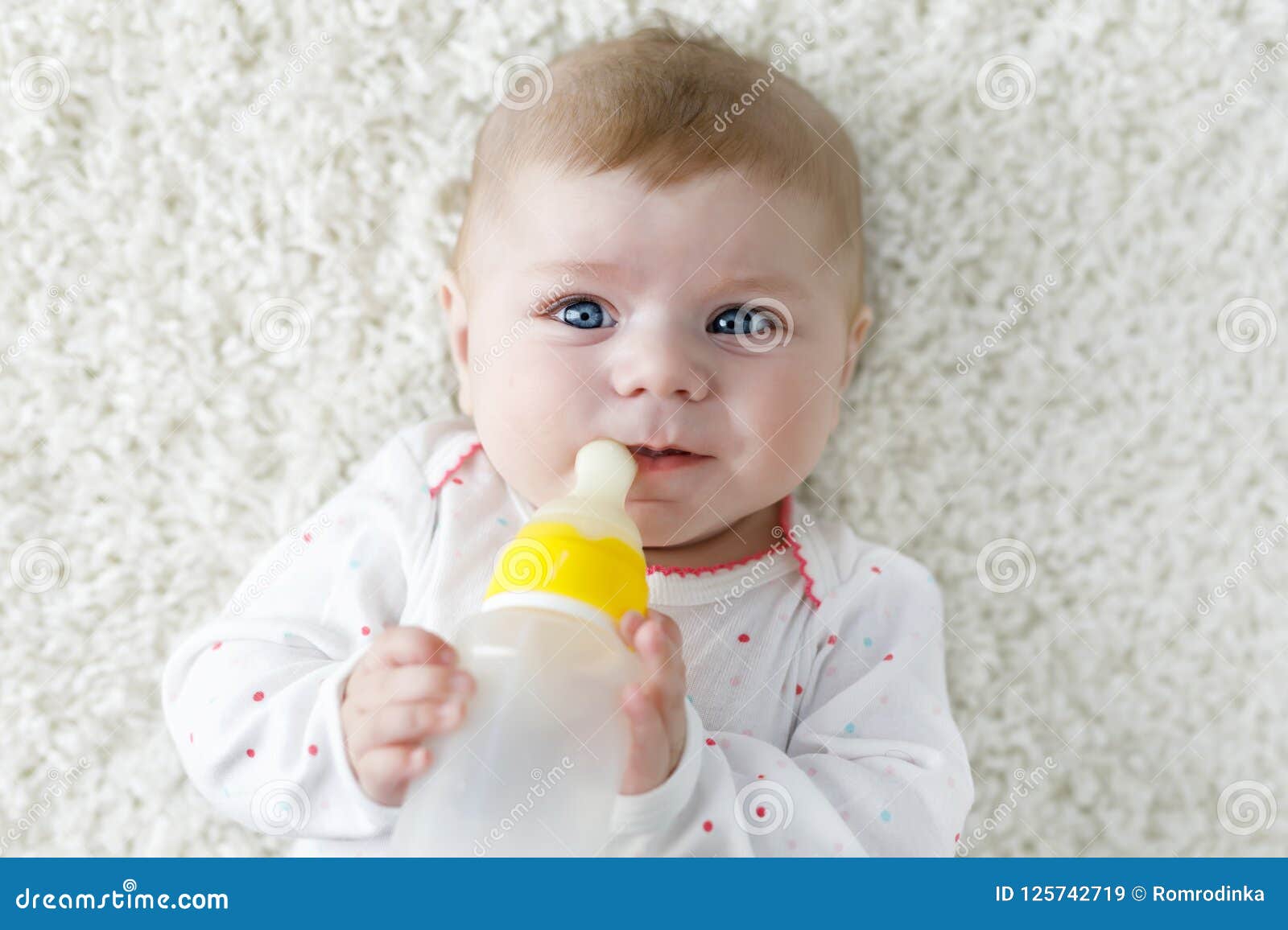 cute adorable ewborn baby girl holding nursing bottle and drinking formula milk. first food for babies. new born child