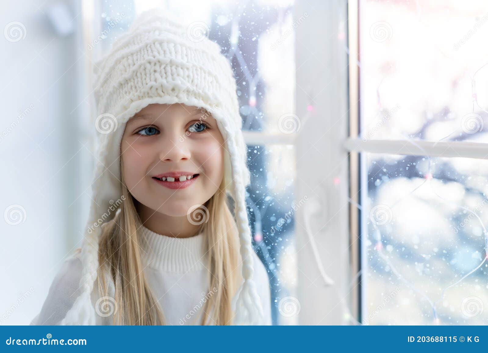 cute adorable little blond beautiful cauasian girl stay near window, dream and looking outside waiting for snow, wonders