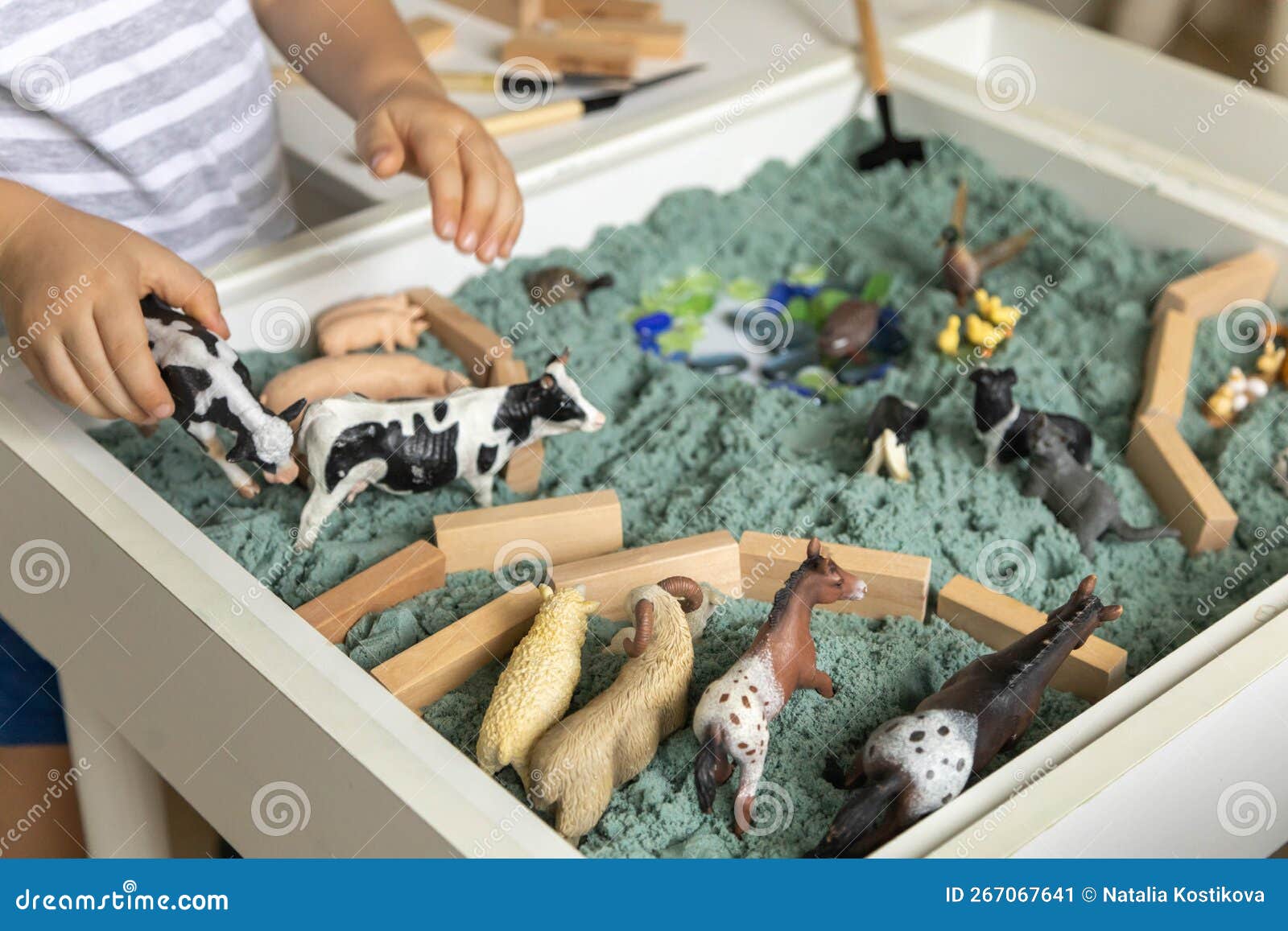 cute baby boy playing sensory box kinetic sand table with farm animals