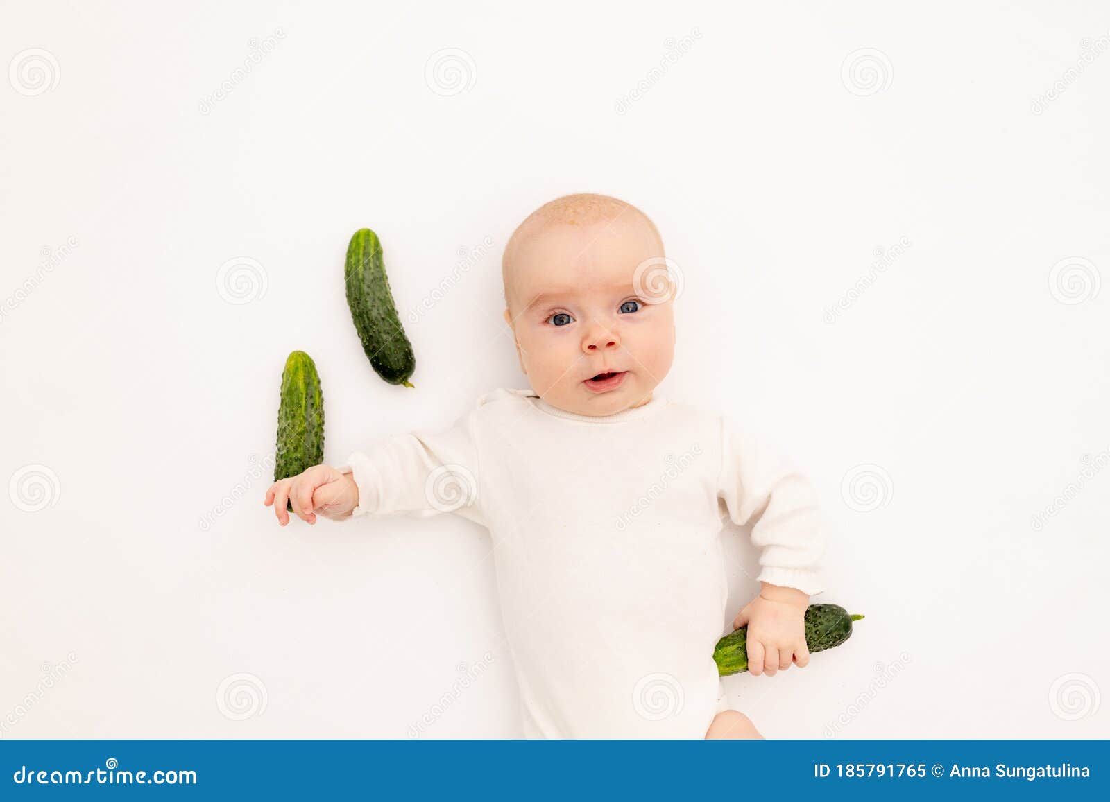 cute baby girl in white boda on a white  background eating cucumbers, first bait, baby 3-6 months among vegetables, space