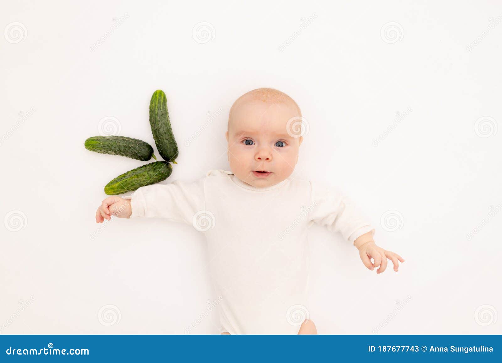 cute baby girl in white boda on a white  background eating cucumbers, first bait, baby 3-6 months among vegetables, space