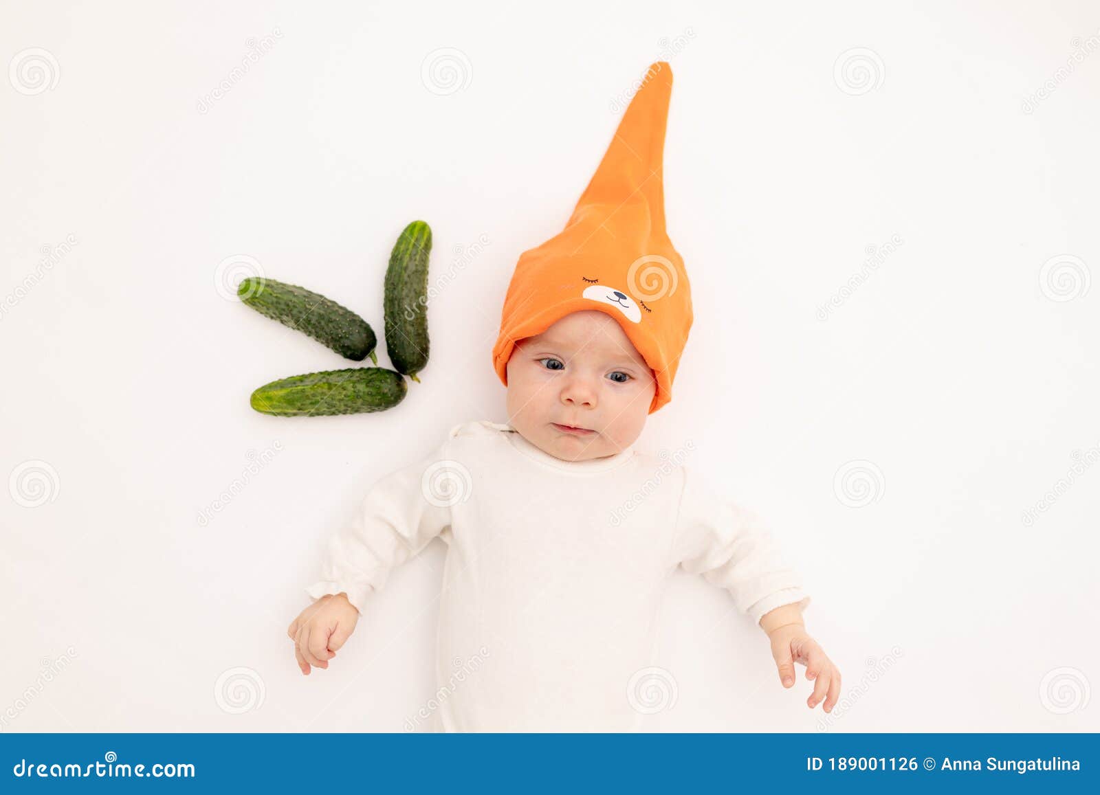 cute baby girl in white boda on a white  background eating cucumbers, first bait, baby 3-6 months among vegetables, space