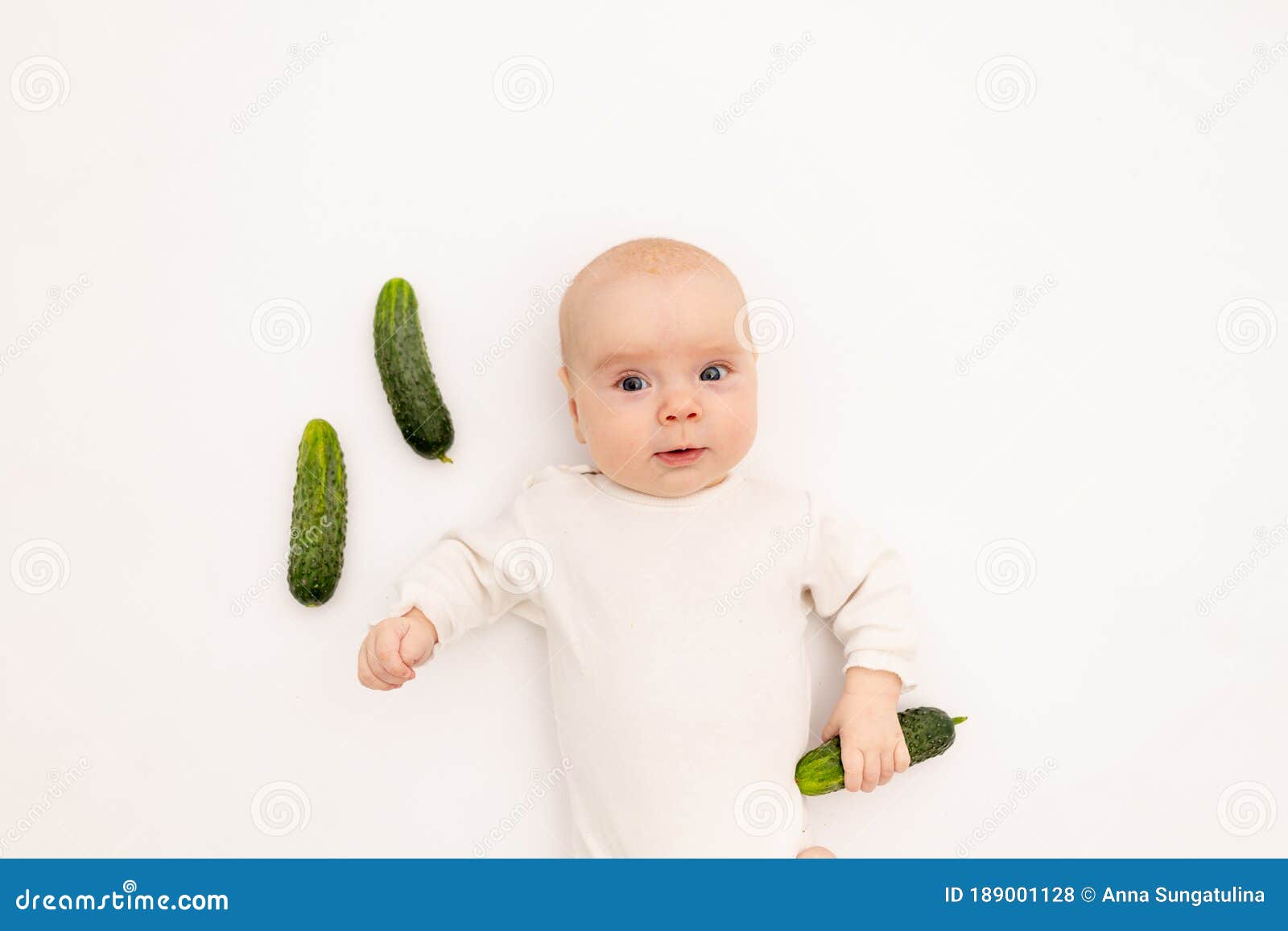 cute baby girl in white boda on a white  background eating cucumbers, first bait, baby 3-6 months among vegetables, space