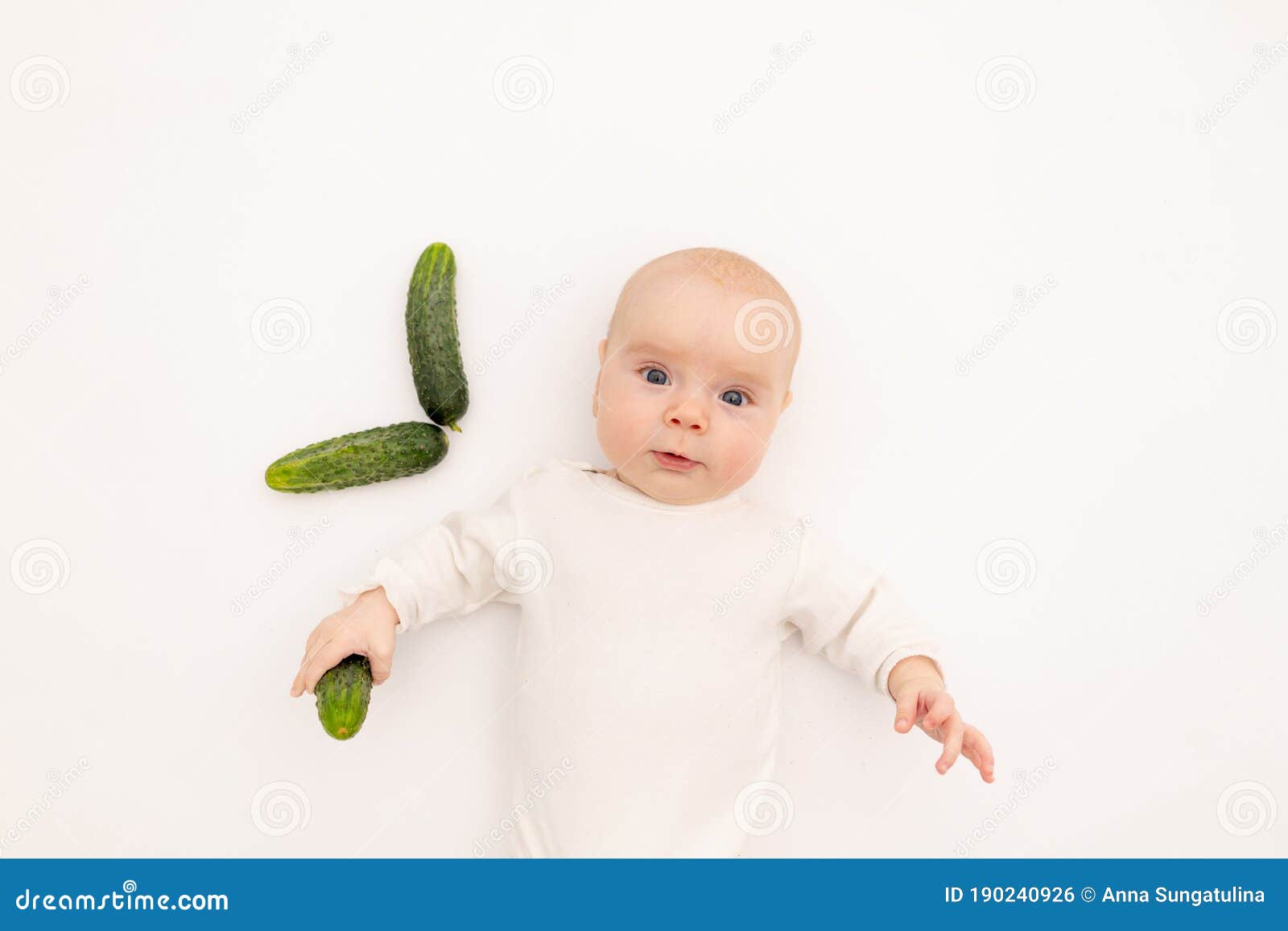 cute baby girl in white boda on a white  background eating cucumbers, first bait, baby 3-6 months among vegetables, space